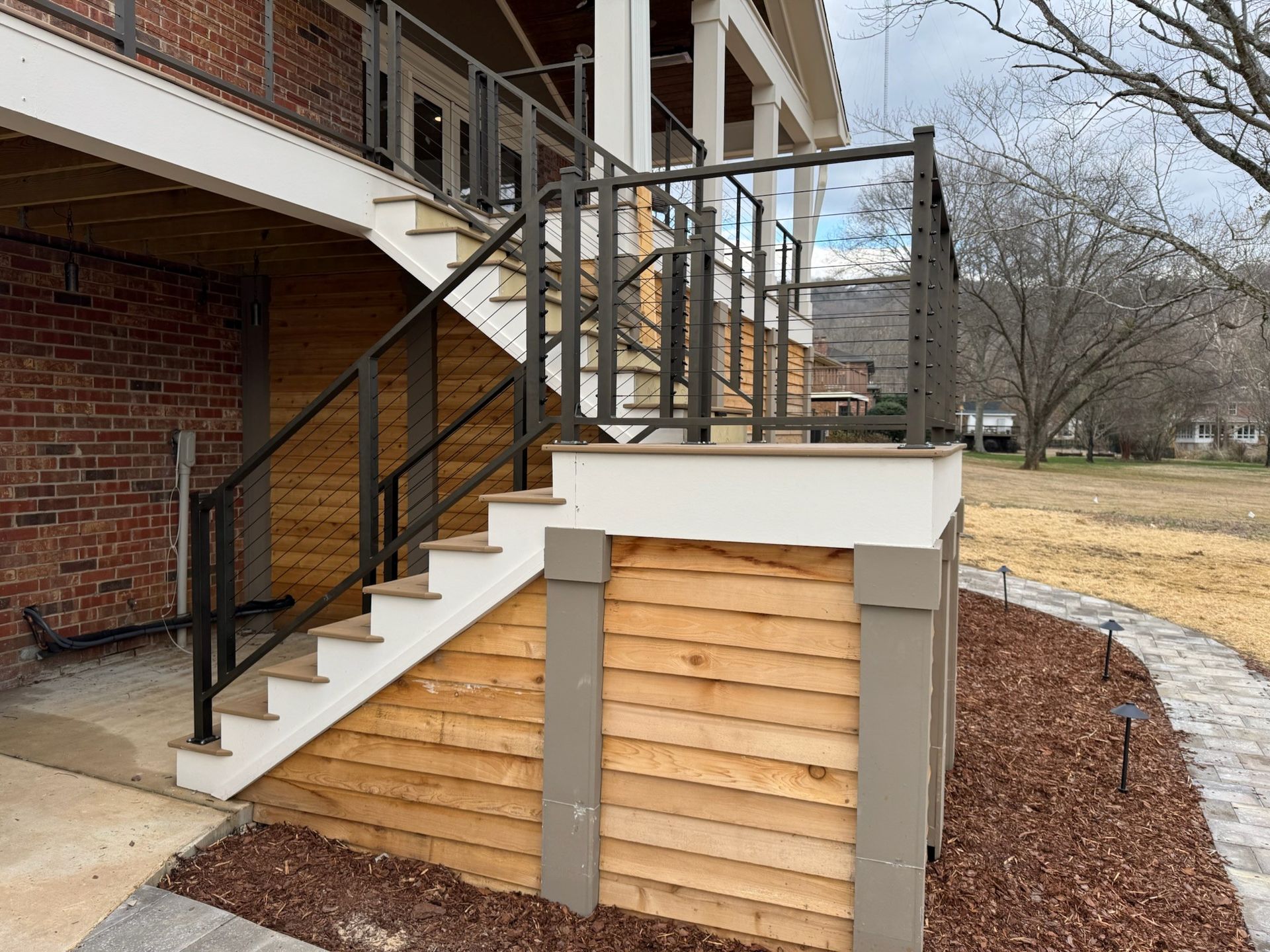 Exterior stairs with metal railings beside a brick building and a wood-paneled utility enclosure.
