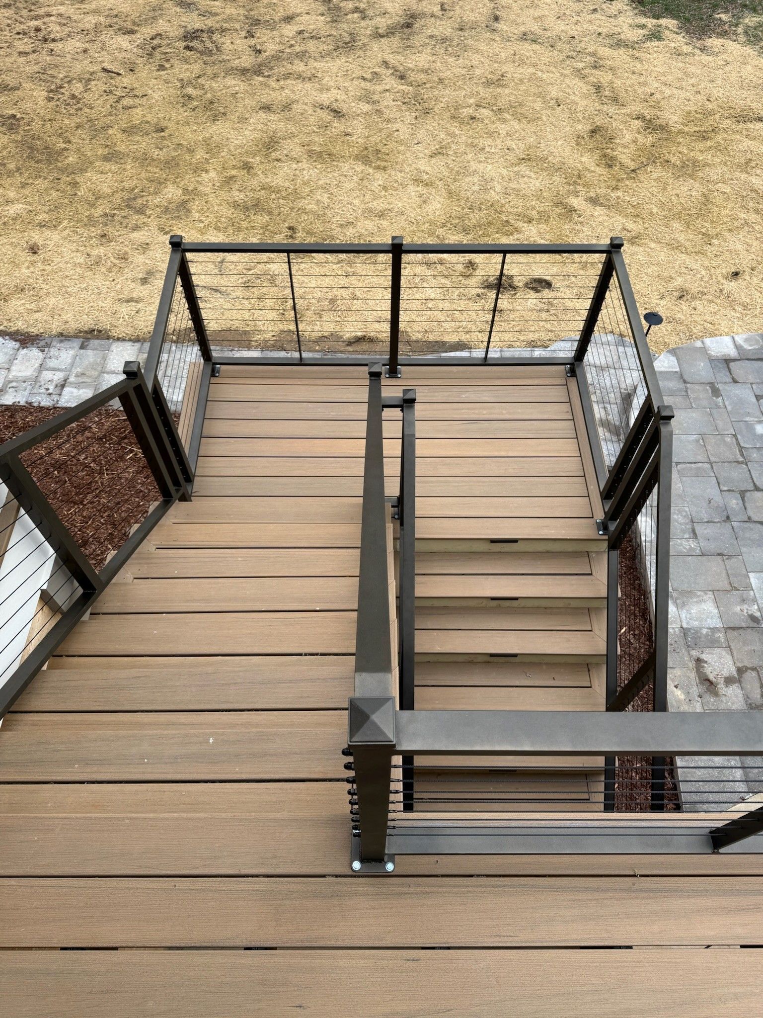 Wooden deck staircase with black railings leading down to a dry grassy yard