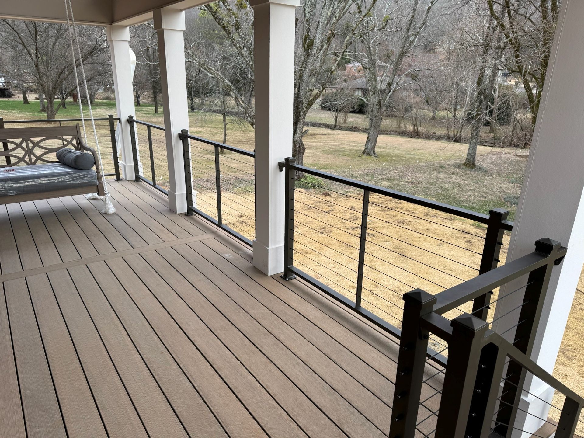 Covered porch with black railings overlooking a grassy yard and leafless trees
