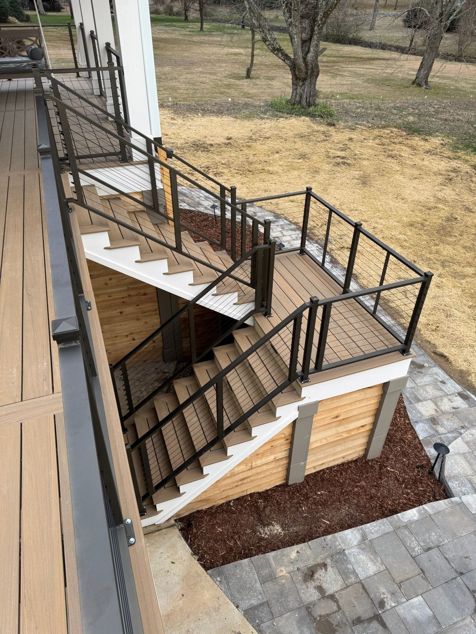 Outdoor staircase with black railings leading to a raised patio beside a building and yard.