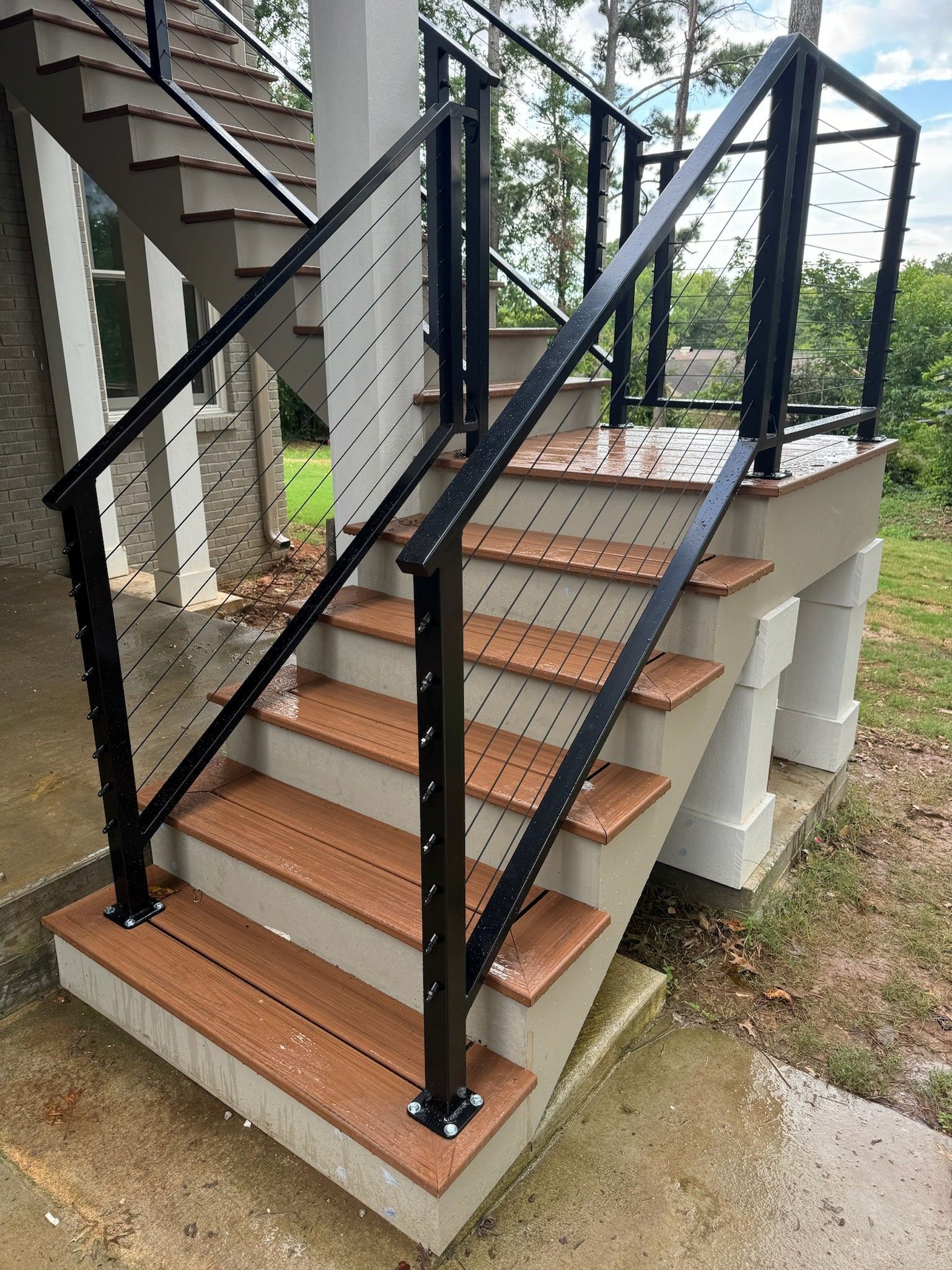 Outdoor wooden stairway with black handrails and a small landing beside a house