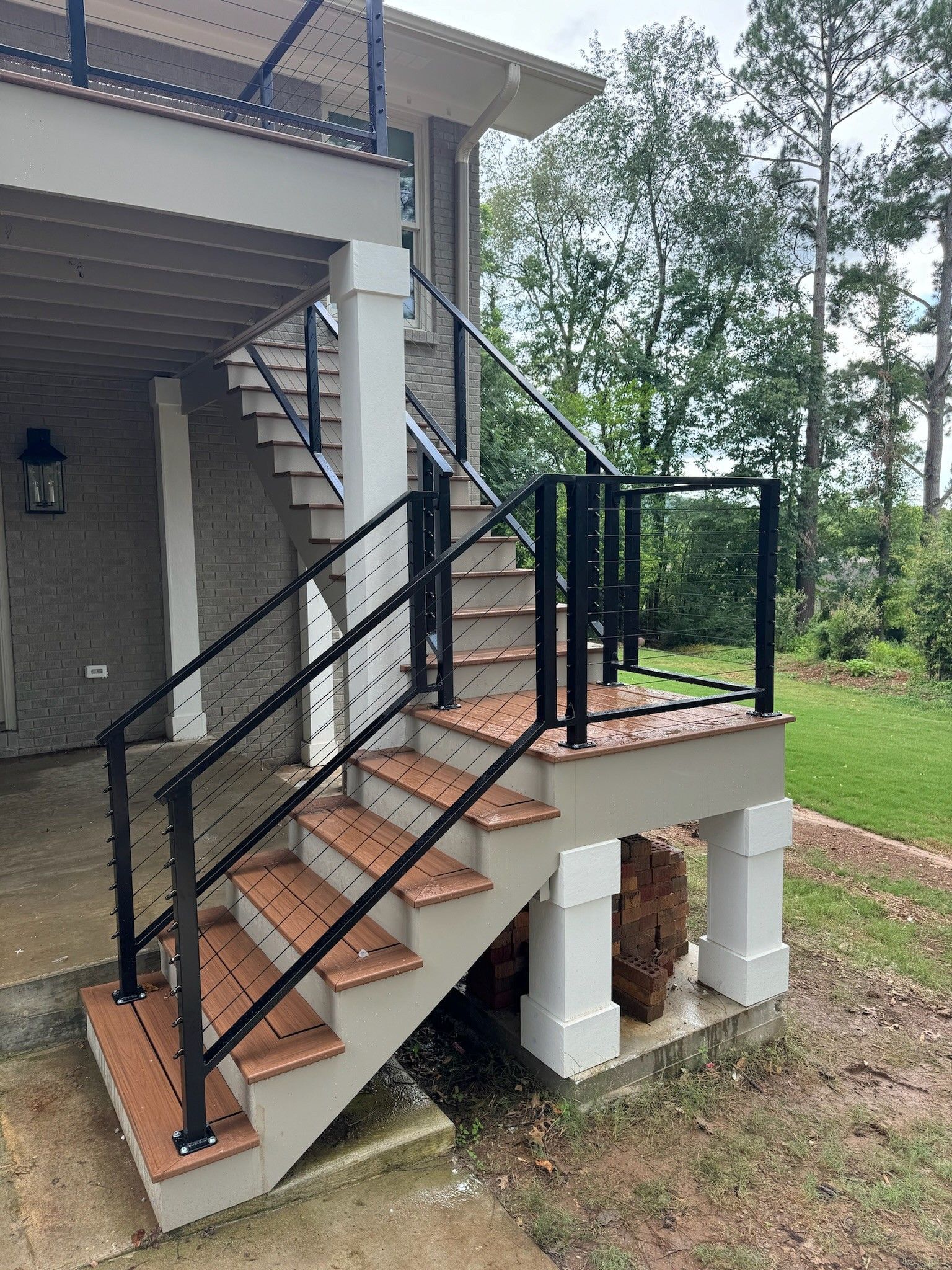 Outdoor concrete staircase with black metal railings leading to a house porch, beside trees and grass.