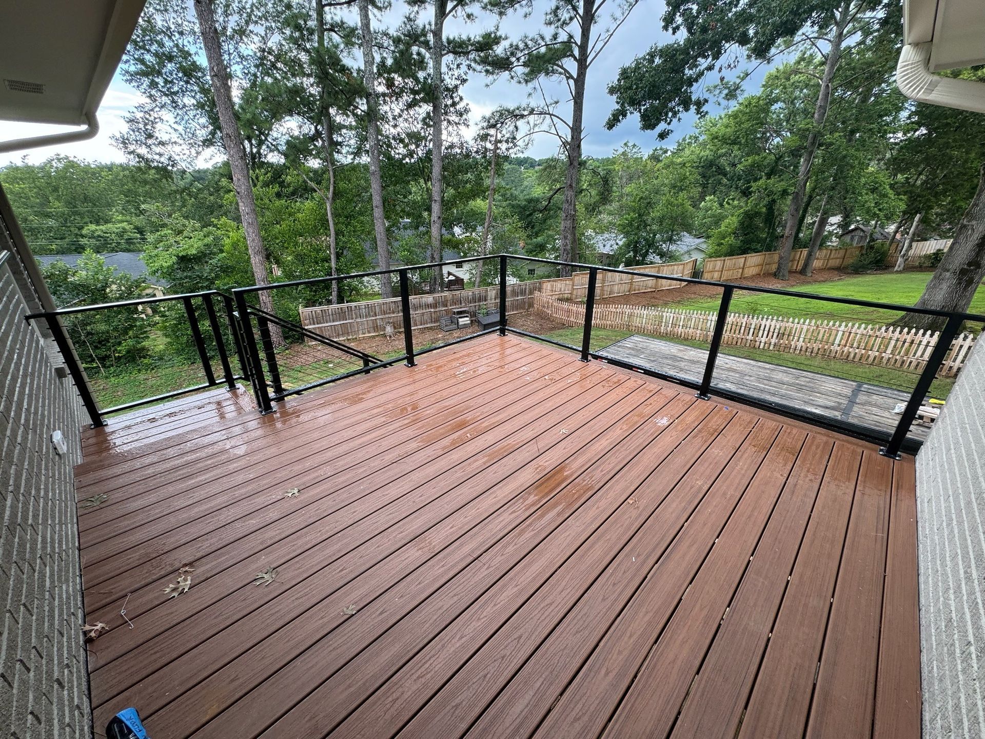 Wooden deck with black railing overlooking a wooded hillside and river.