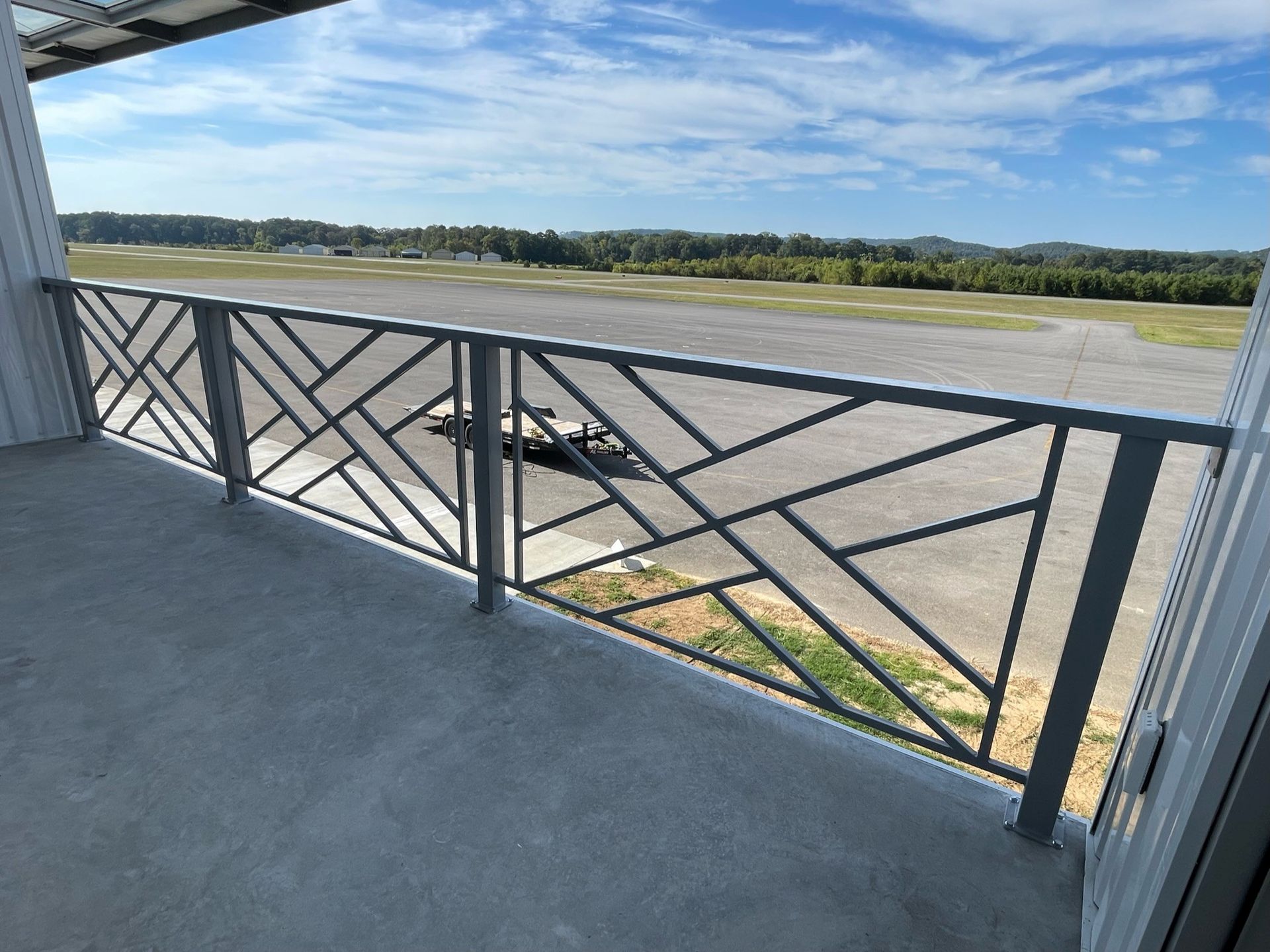 Black metal railing on a concrete balcony overlooking an open airfield and green landscape.
