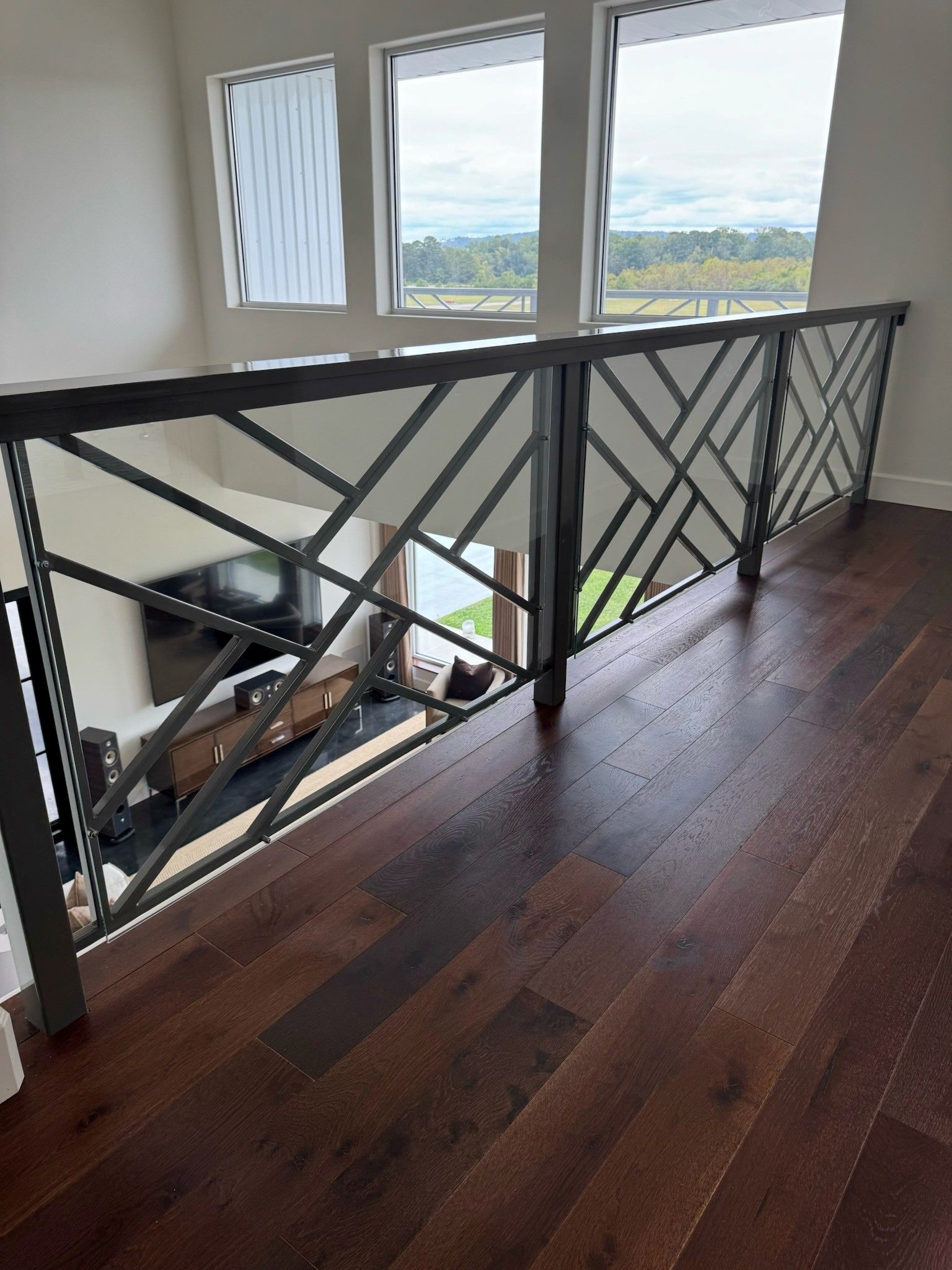 Modern stair landing with dark wood floor, black railing, and large windows overlooking a landscape