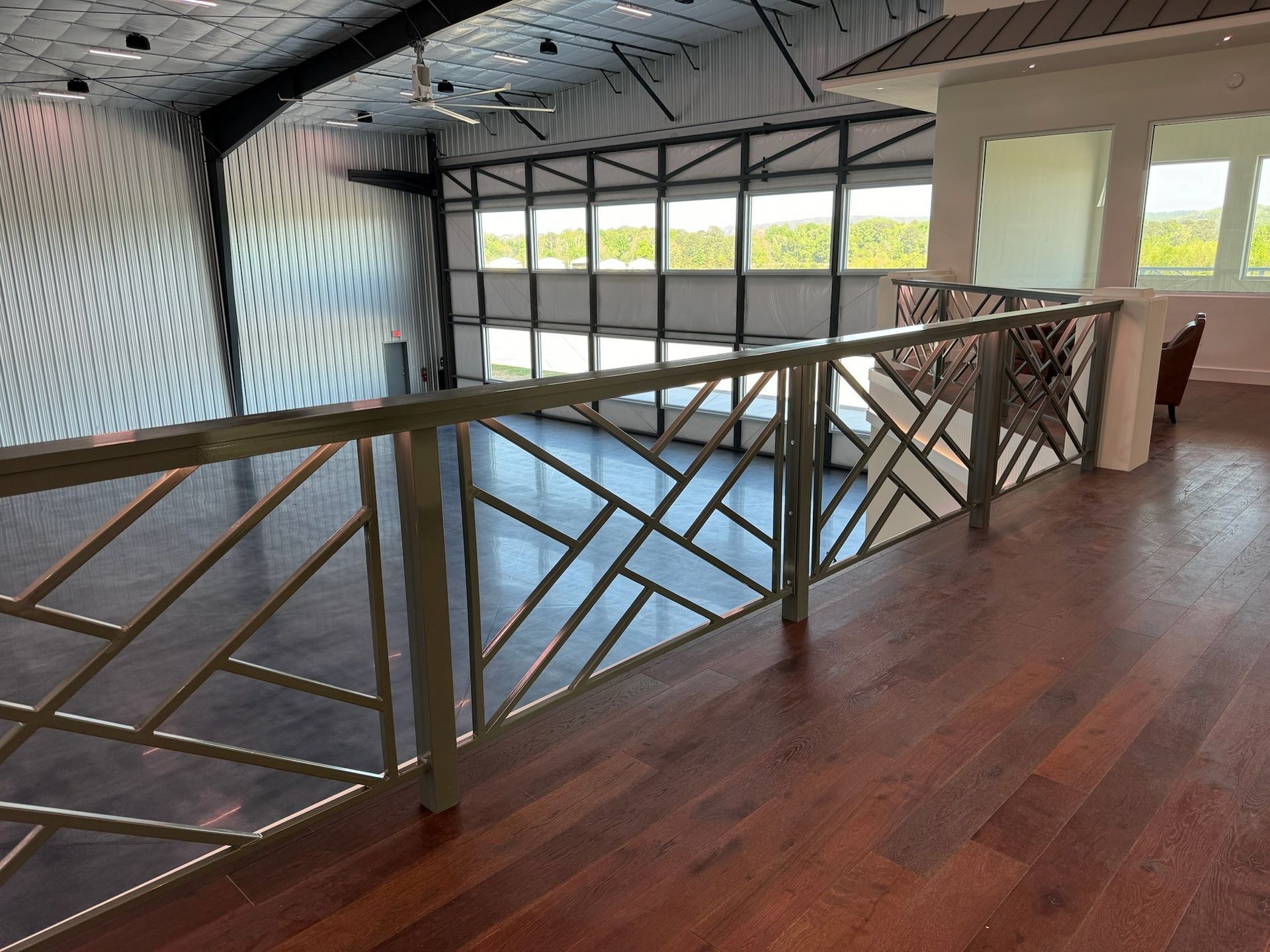 Indoor loft walkway with metal railing, wood floor, and large windows overlooking a gym space