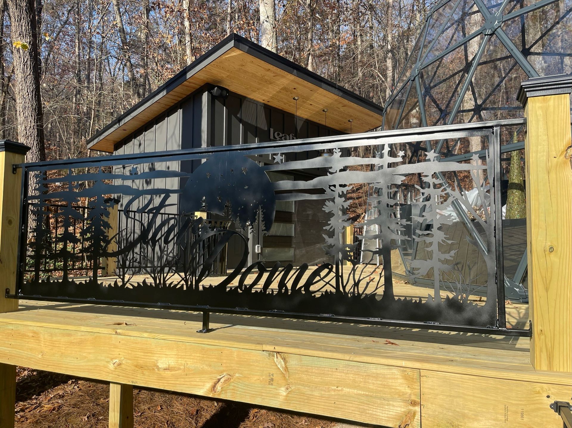 Modern house with black metal fence and frosted glass panels on a wooden deck in a wooded setting