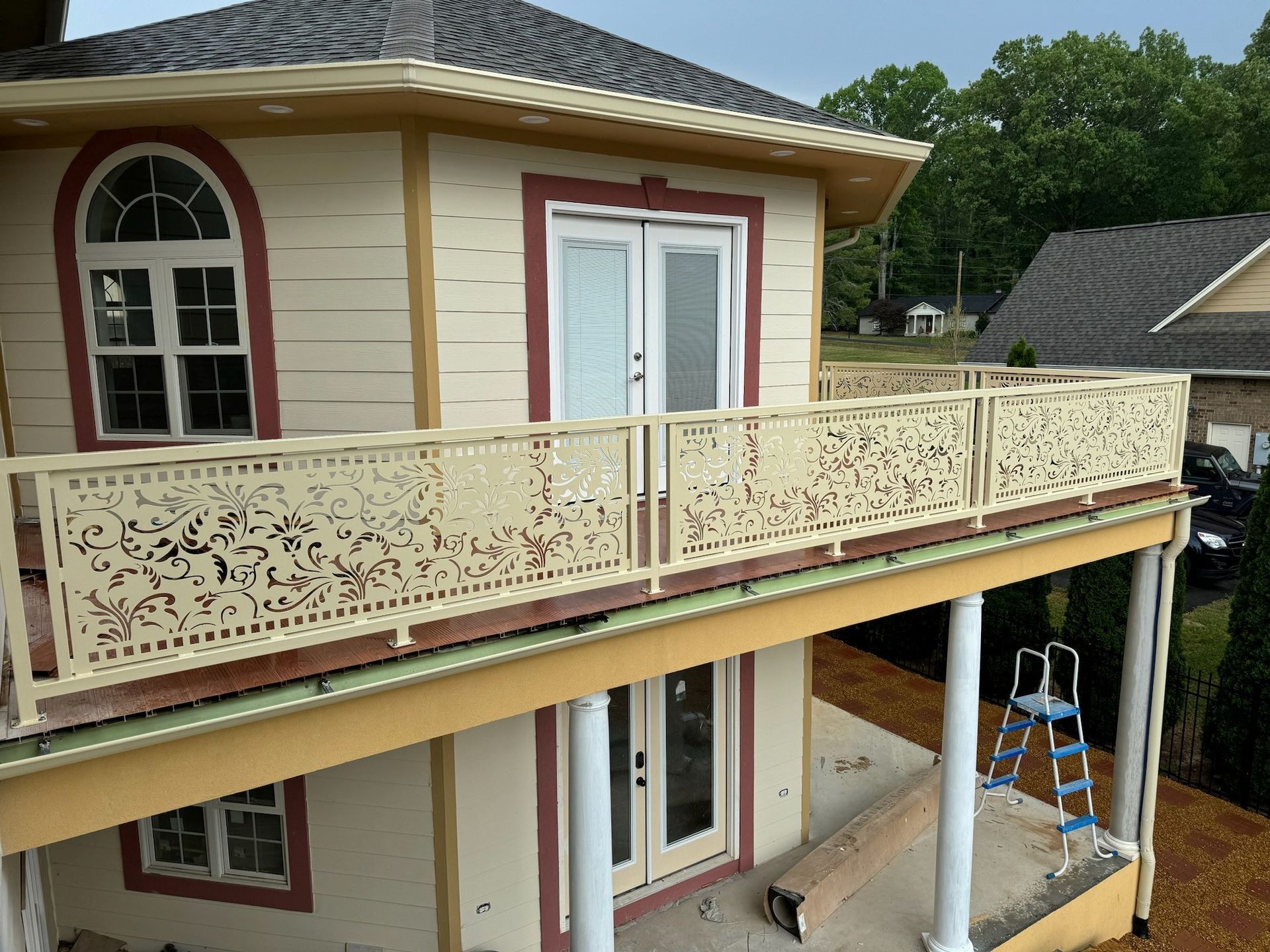 House exterior with an ornate beige balcony and red-trimmed doors, viewed from the side during construction