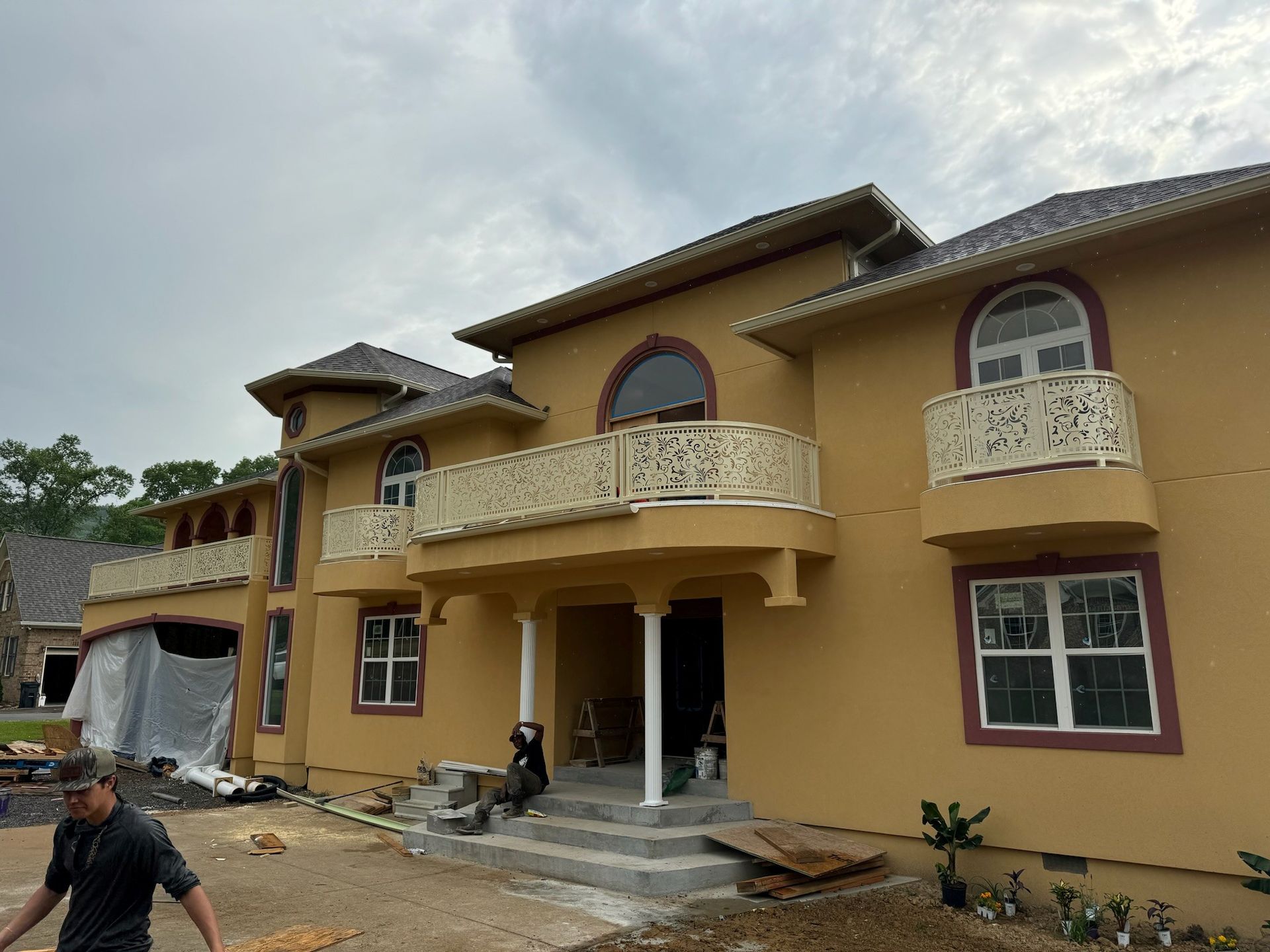 Two-story beige house with balconies, white trim, and workers finishing the front entrance.