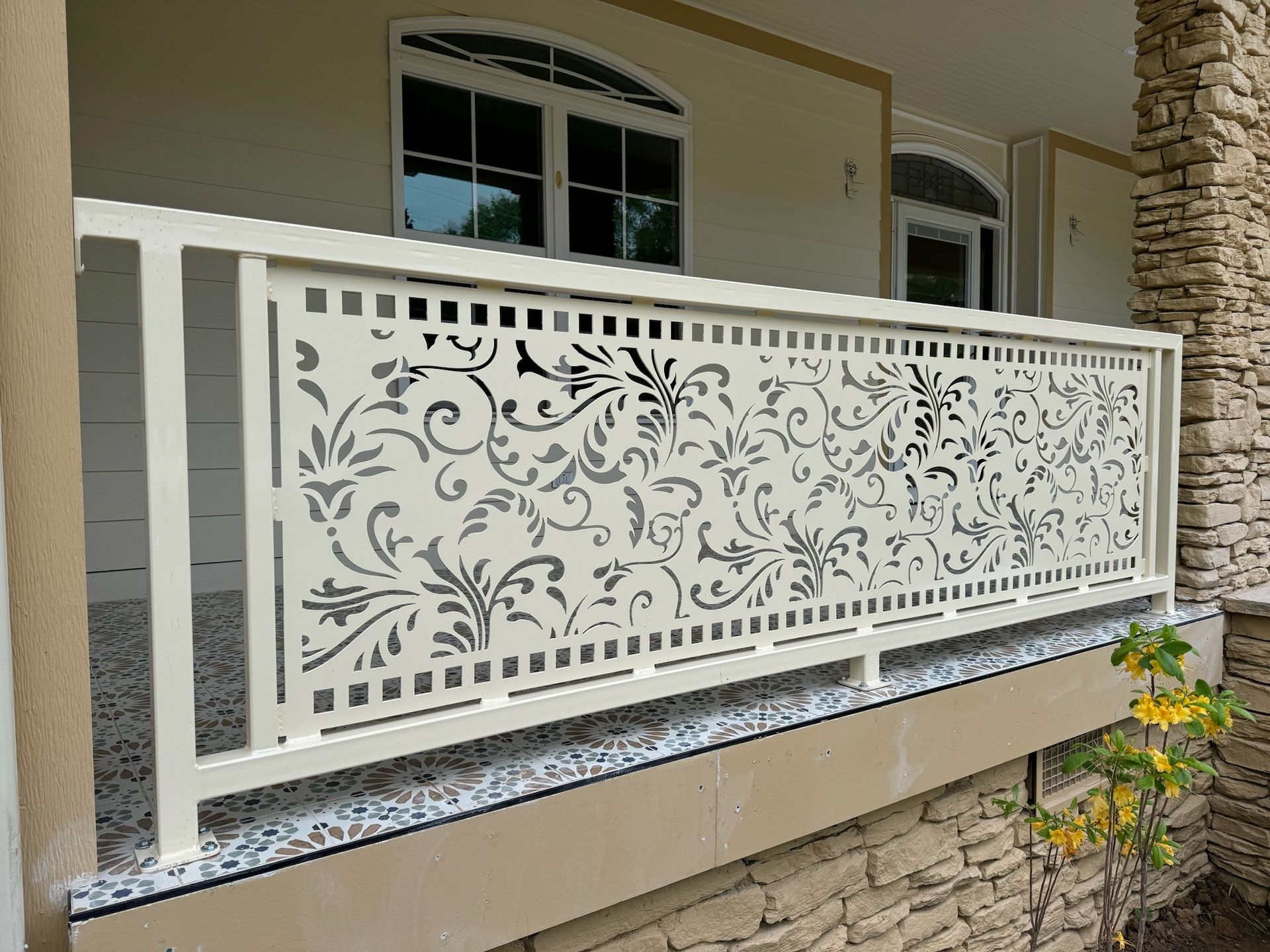 White balcony railing with decorative floral metal panel outside a beige house.