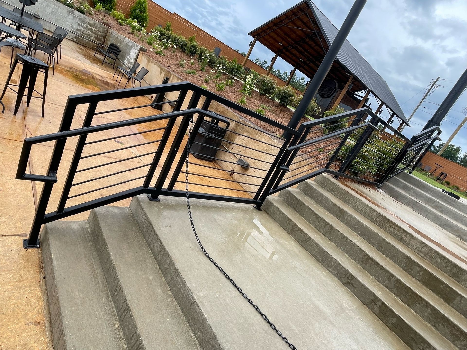 Outdoor ramp and stairs with black metal railings beside a brick building on a cloudy day