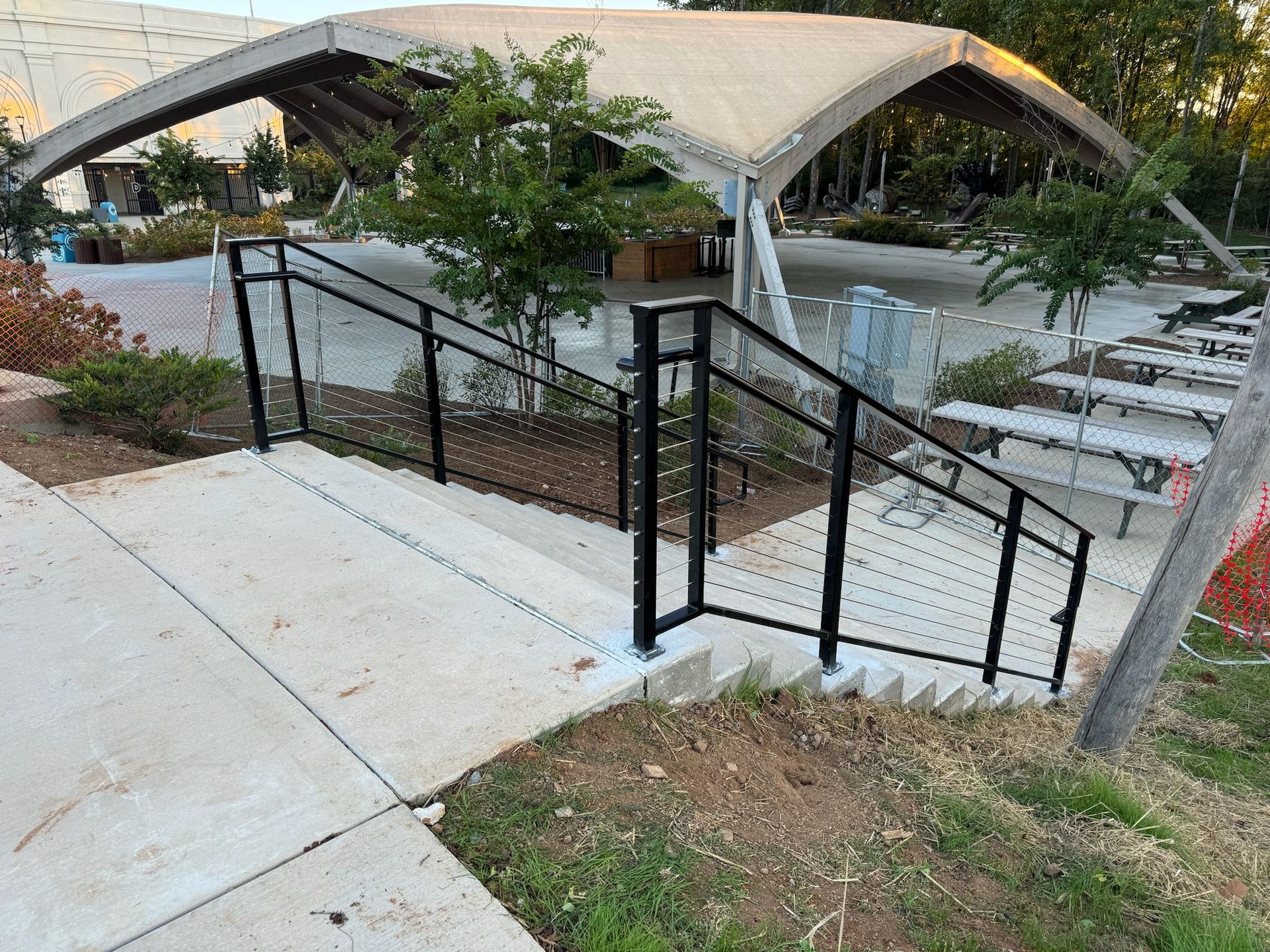 Outdoor stairs with black railings beside a concrete path, leading to a waterfront area under arched canopies