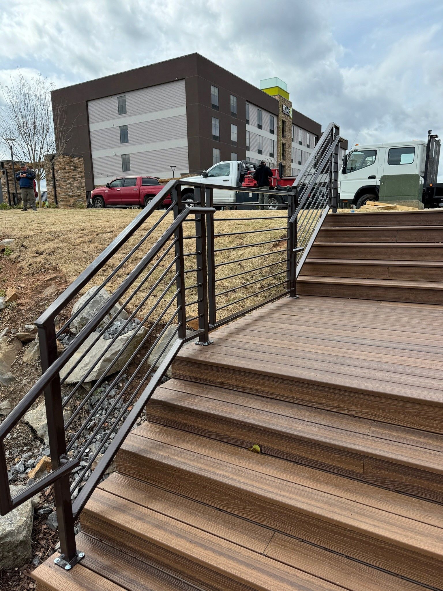 Outdoor staircase with black railings and metal steps beside a brick building and white truck at a construction site