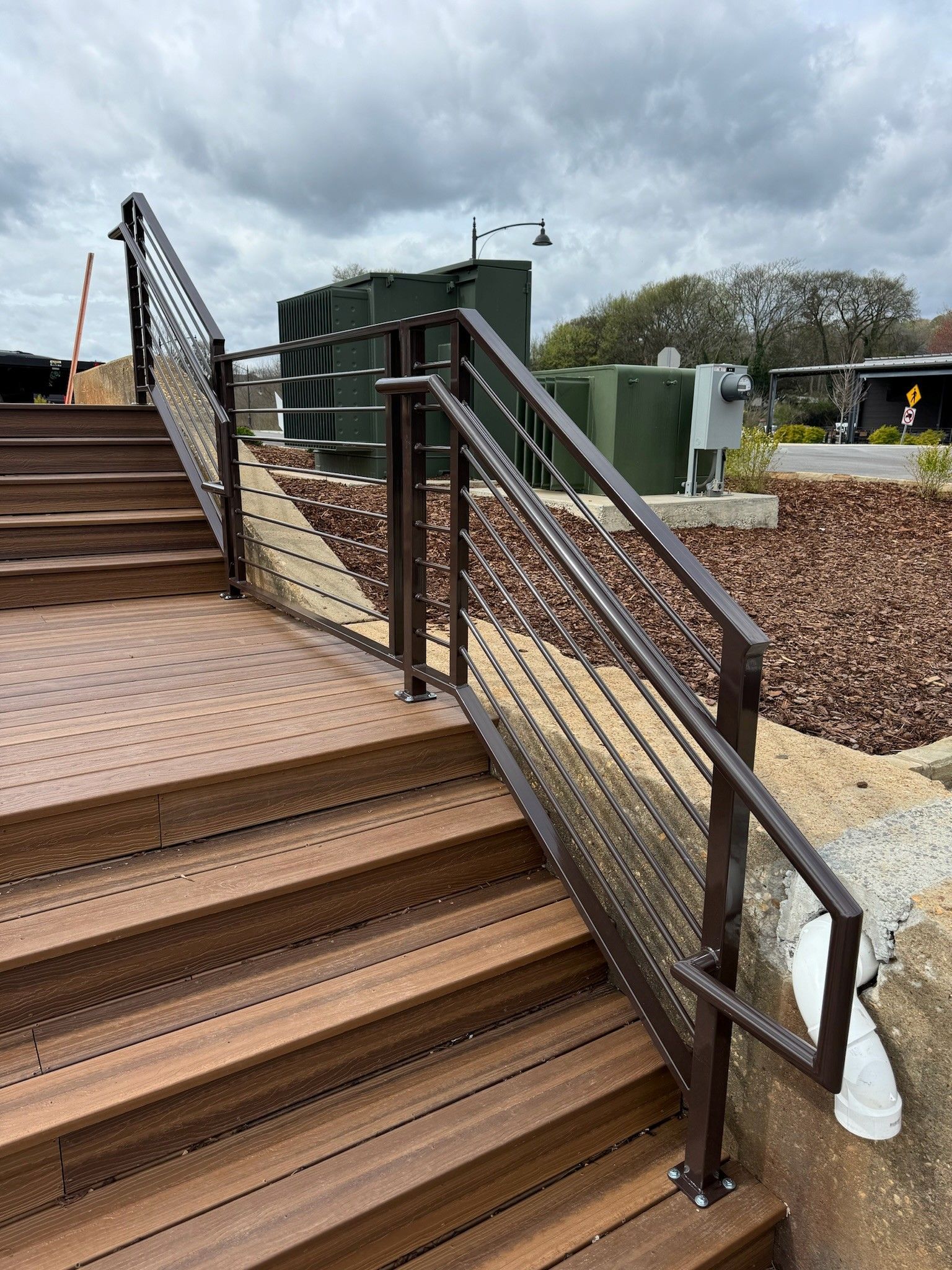 Rust-colored metal stairs with handrails beside an outdoor industrial site under a cloudy sky
