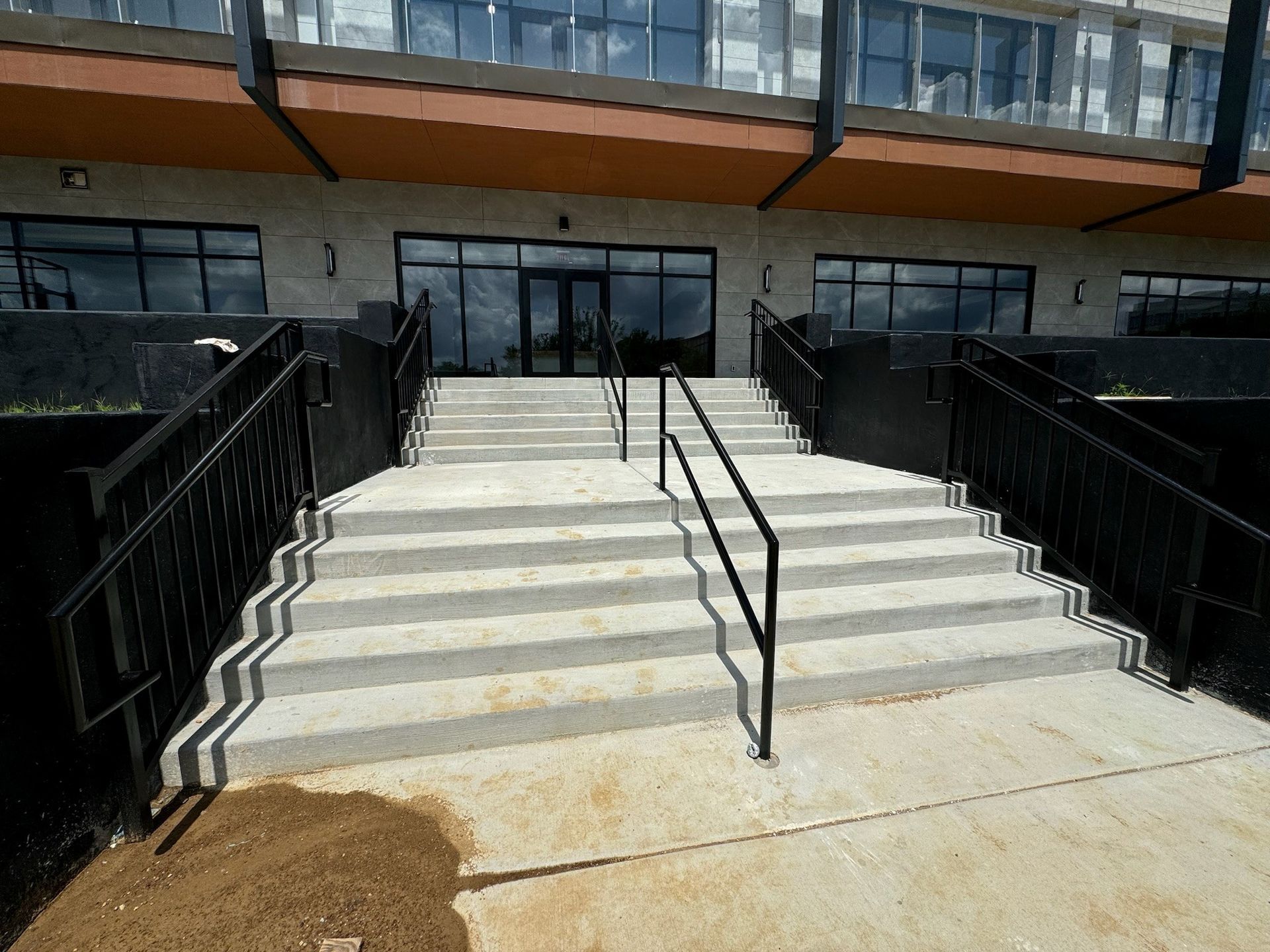 Concrete stairs leading to a building entrance with black railings and glass doors