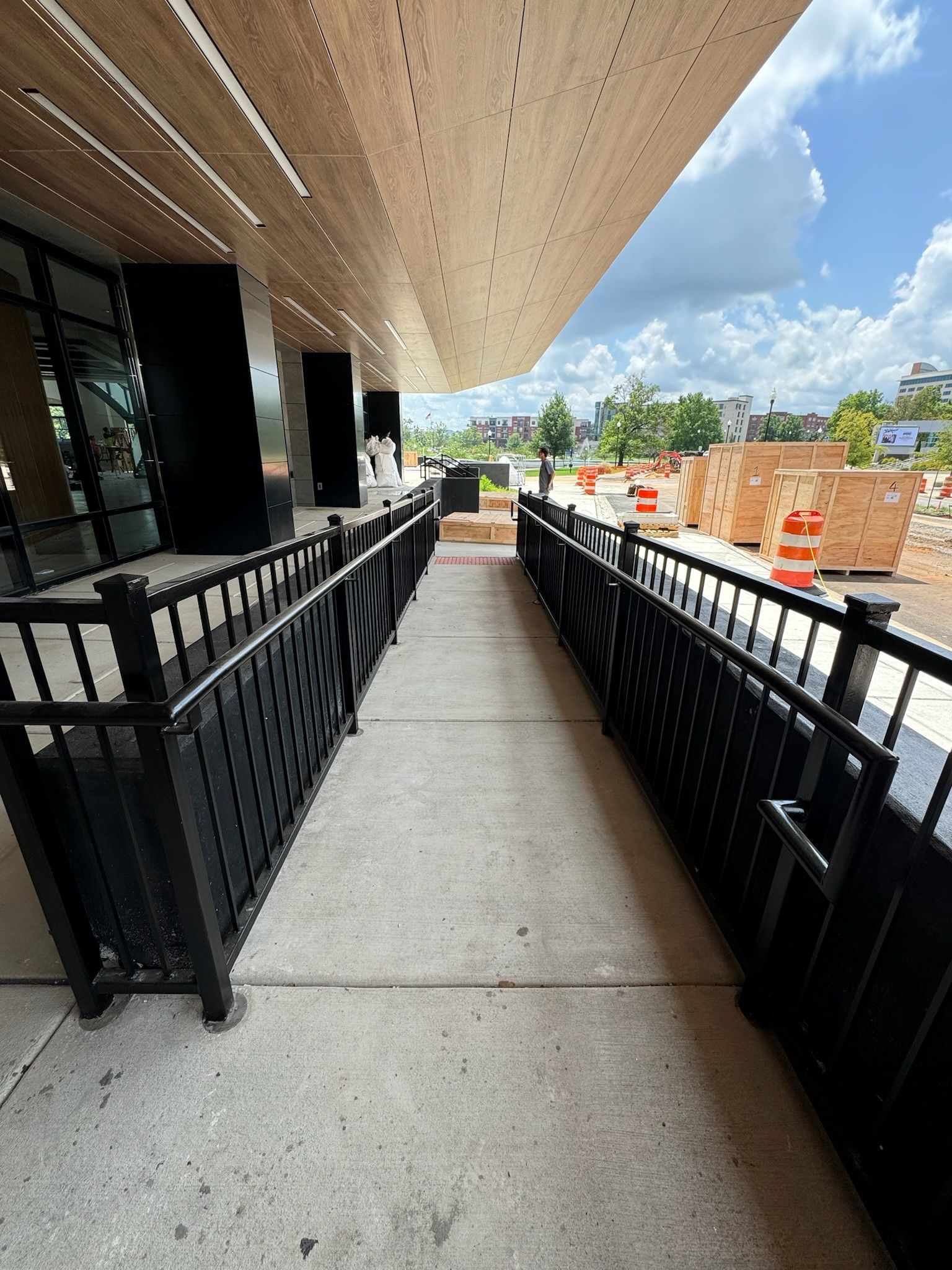 Covered entrance ramp with black railings leading to a building under construction on a sunny day