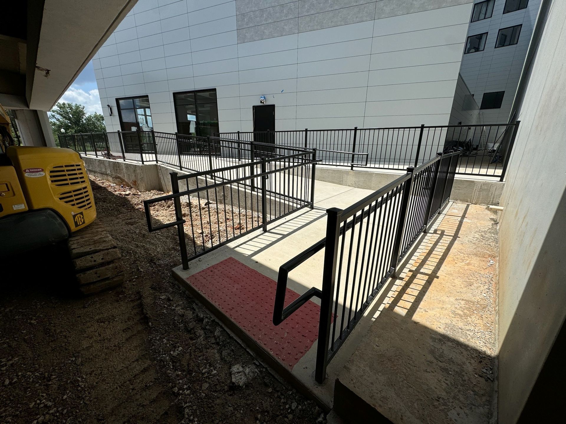 Accessible ramp with black railings and a red mat beside a building entrance
