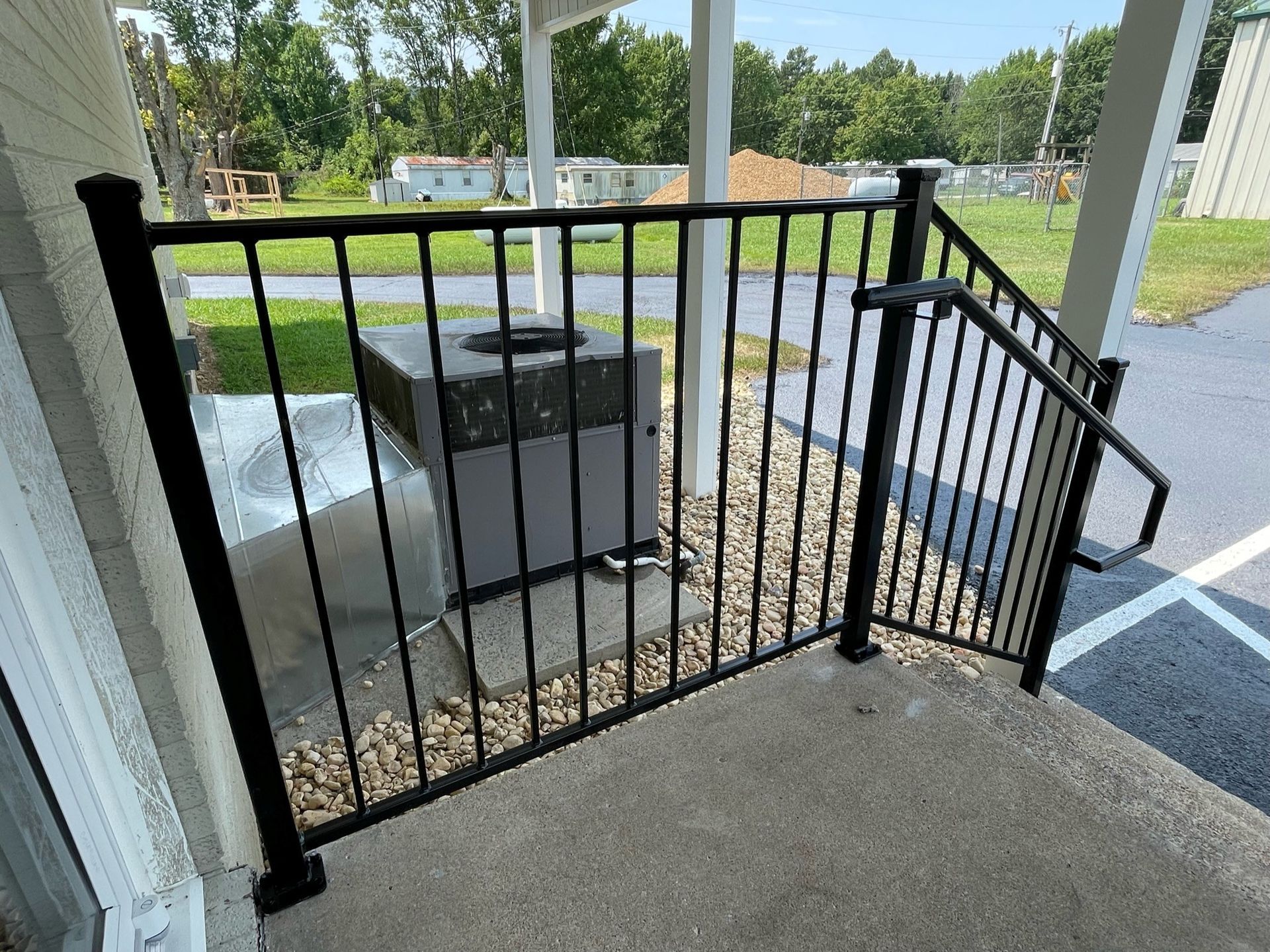 Black metal gate and railing on a porch, with an outdoor HVAC unit beyond it.