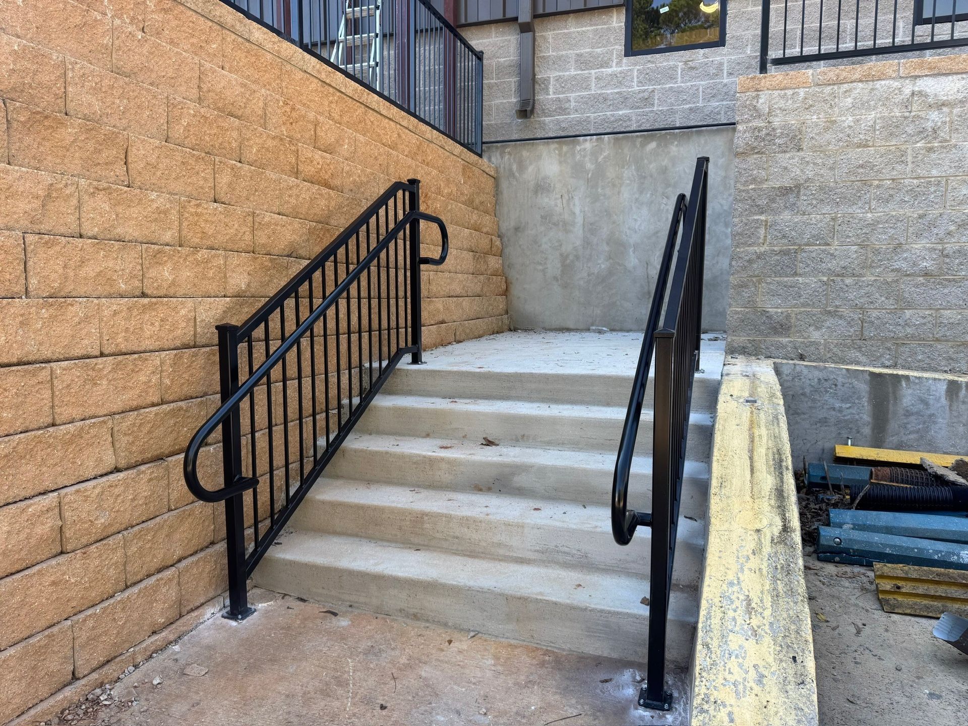 Concrete outdoor staircase with black railings between brick and gray walls