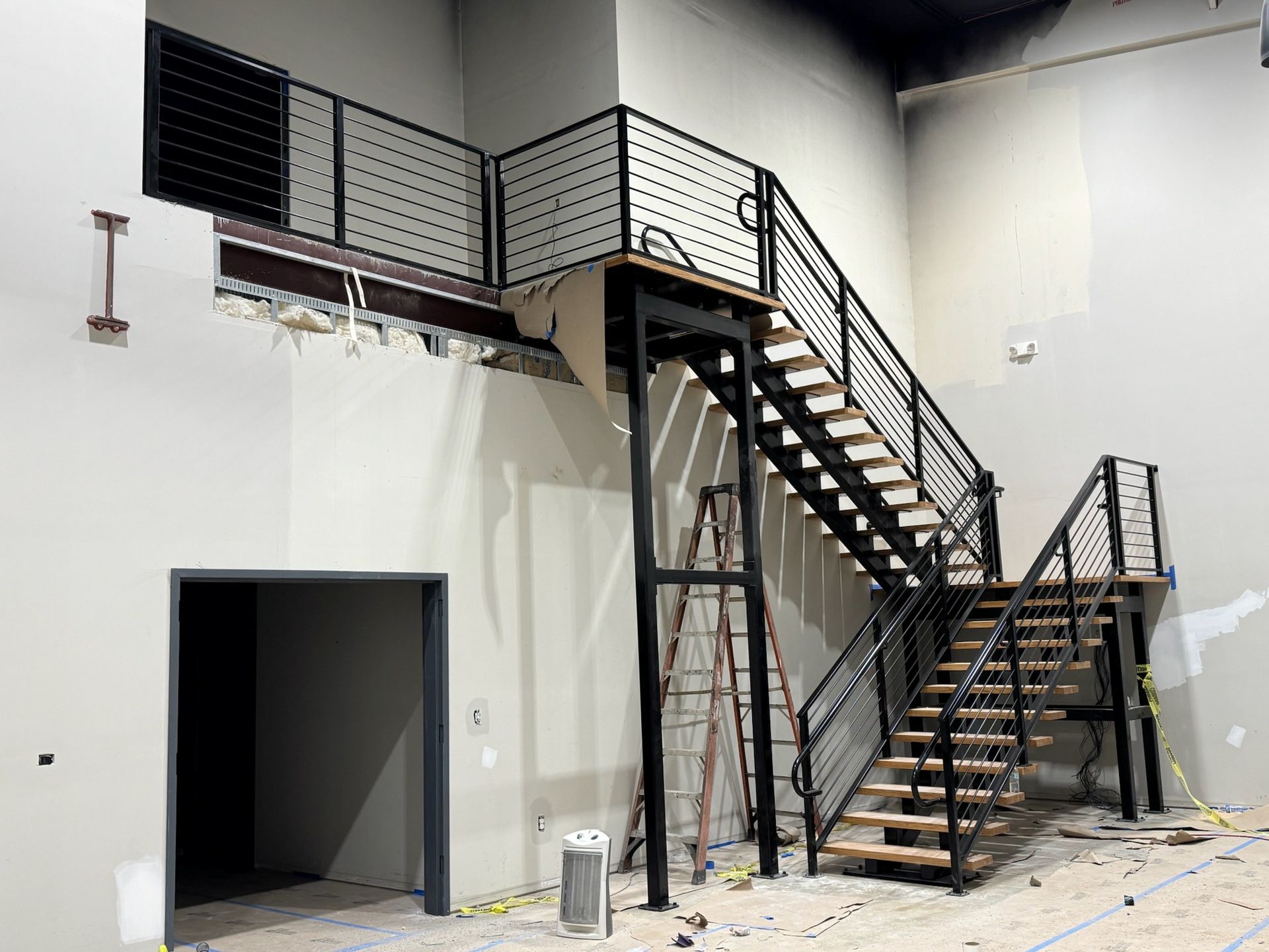 Empty industrial room with black metal stairs and mezzanine walkway along white walls
