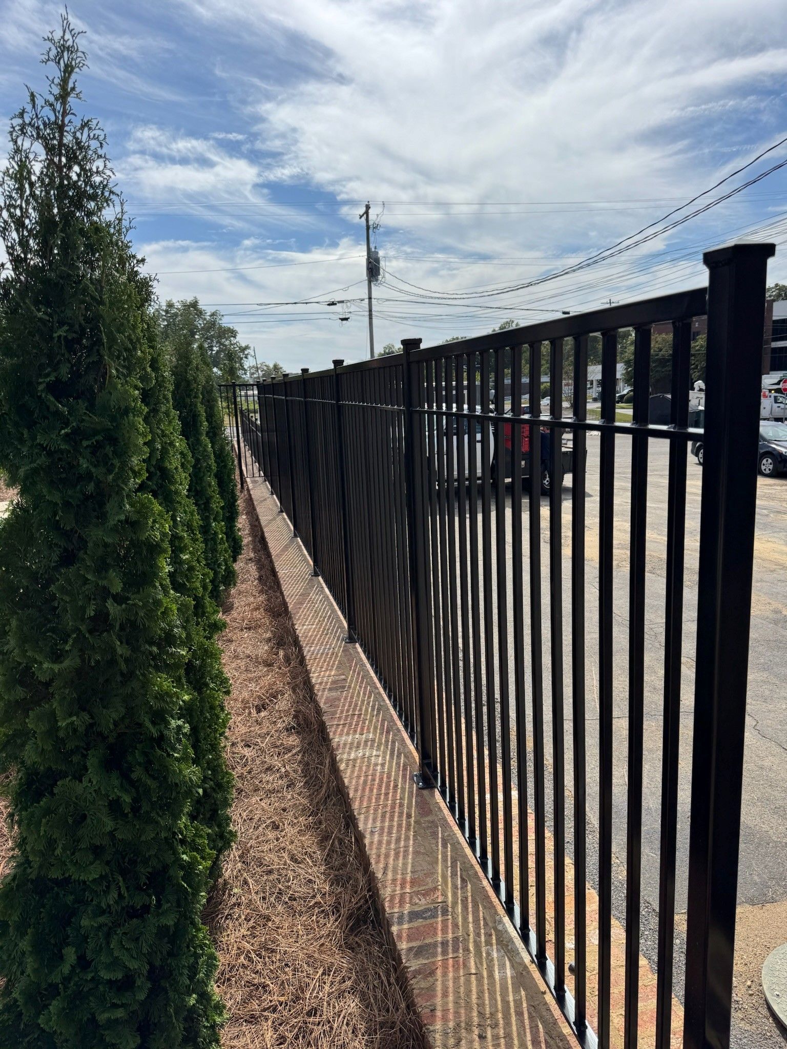 Black metal fence beside a sidewalk and shrubs under a partly cloudy sky
