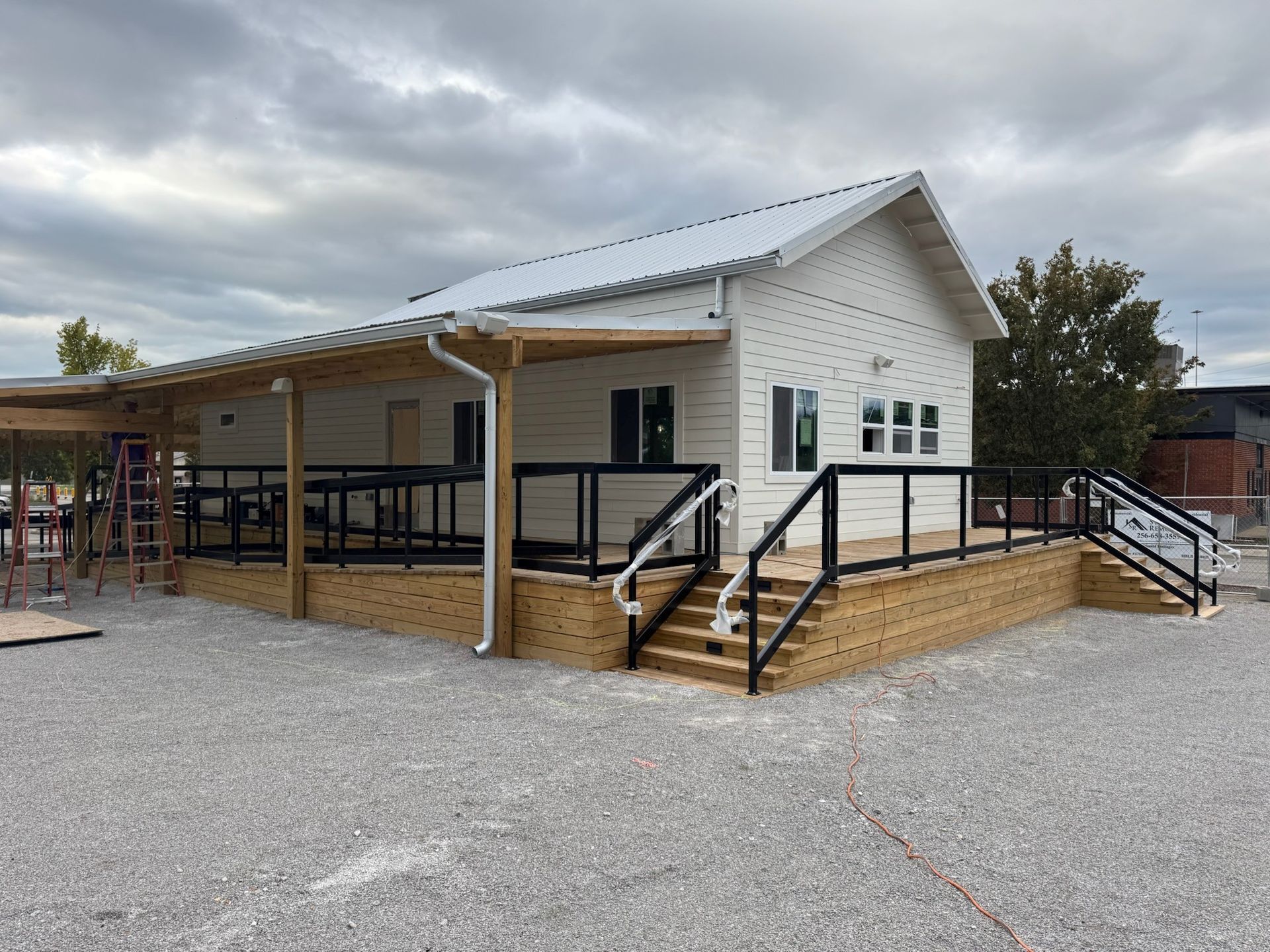 White-sided building with covered porch, black railings, and gravel driveway