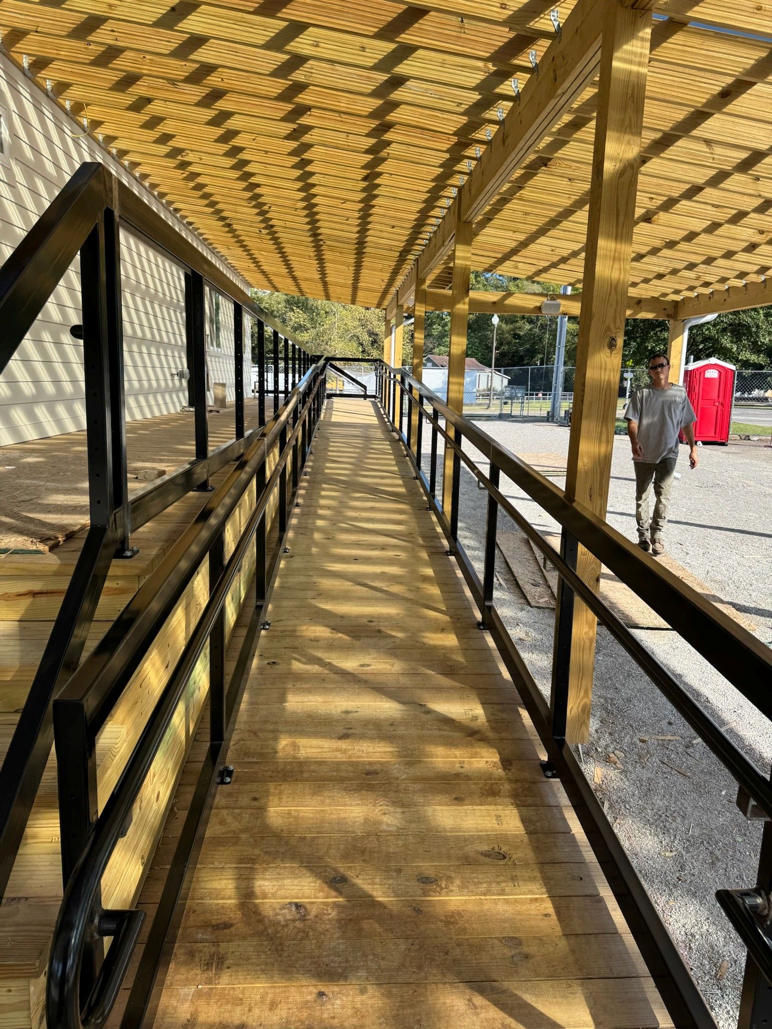 Covered walkway with black railings and patterned canopy casting shadows, with a person in red nearby