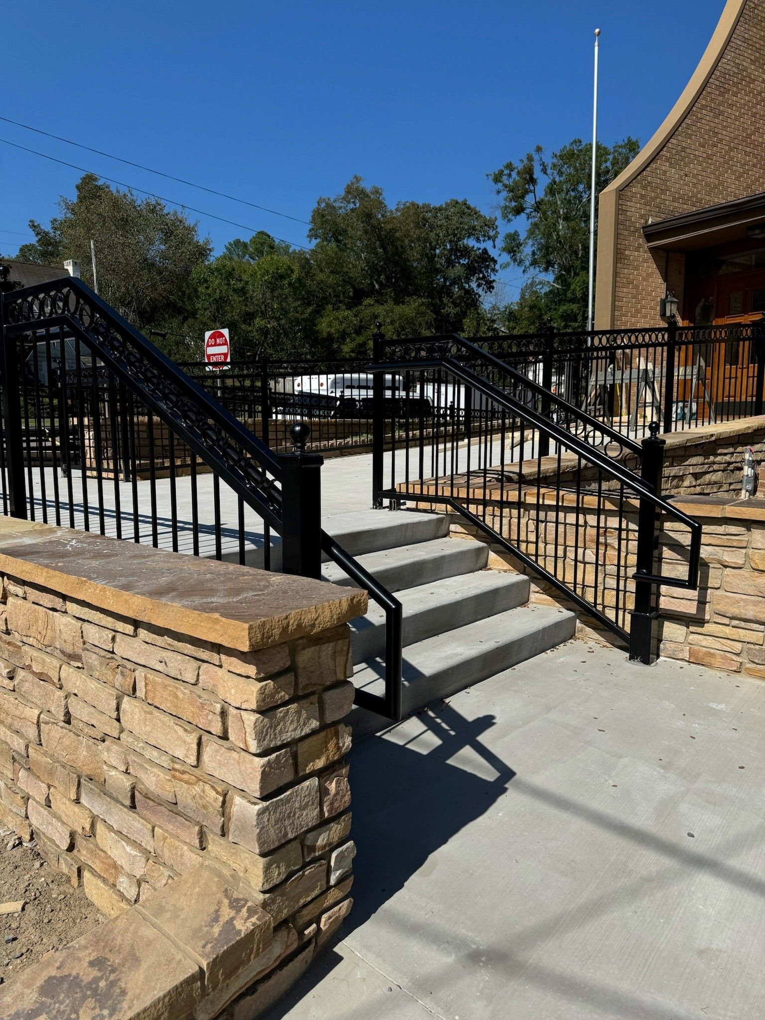 Brick ramp and stairs with black railings leading to a building entrance under a clear blue sky.