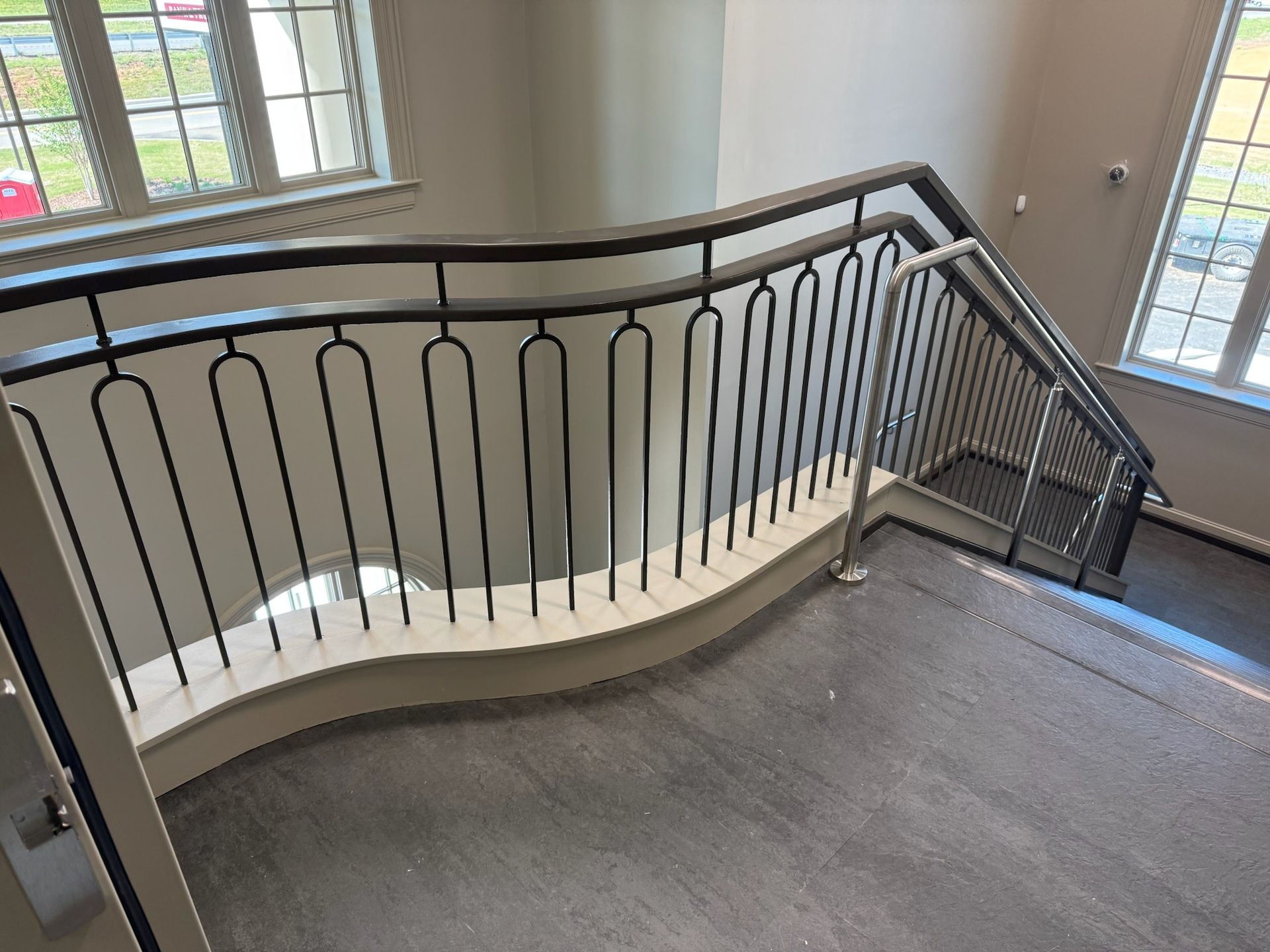 Interior staircase landing with black railing, gray carpet, and windows