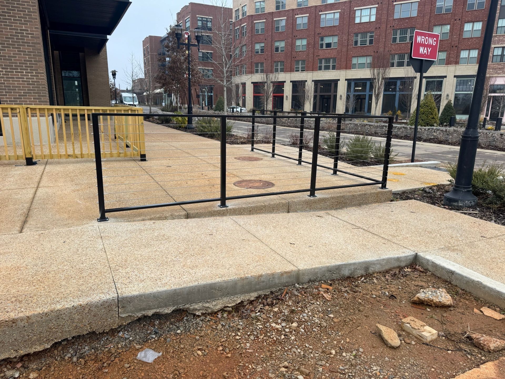 Urban sidewalk ramp with black railings, concrete curb, and apartment buildings in the background