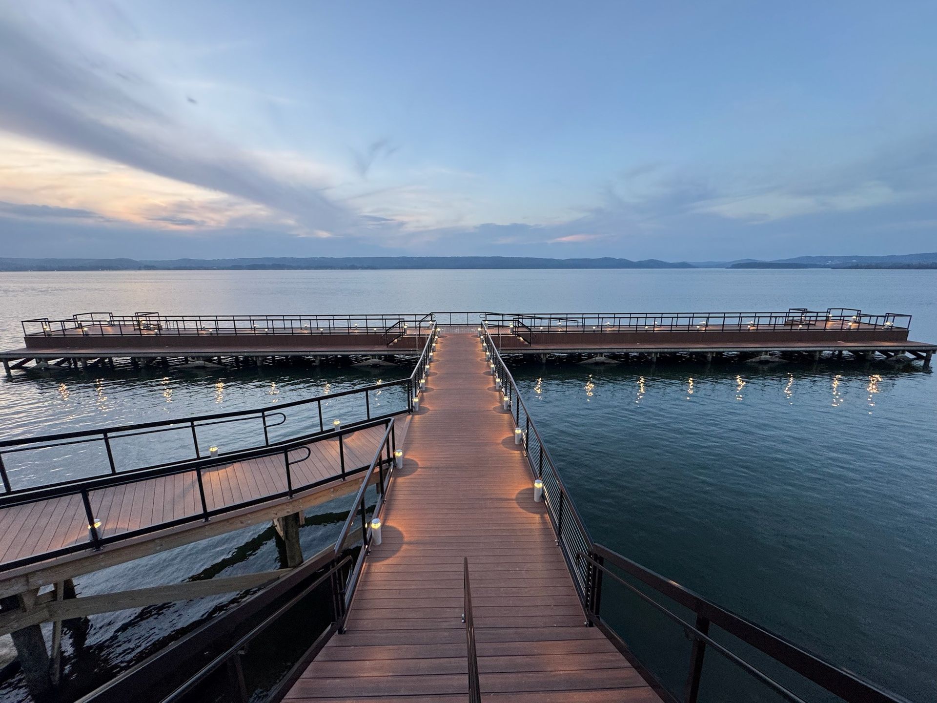 Wooden pier stretching into calm water at sunset under a blue, cloudy sky