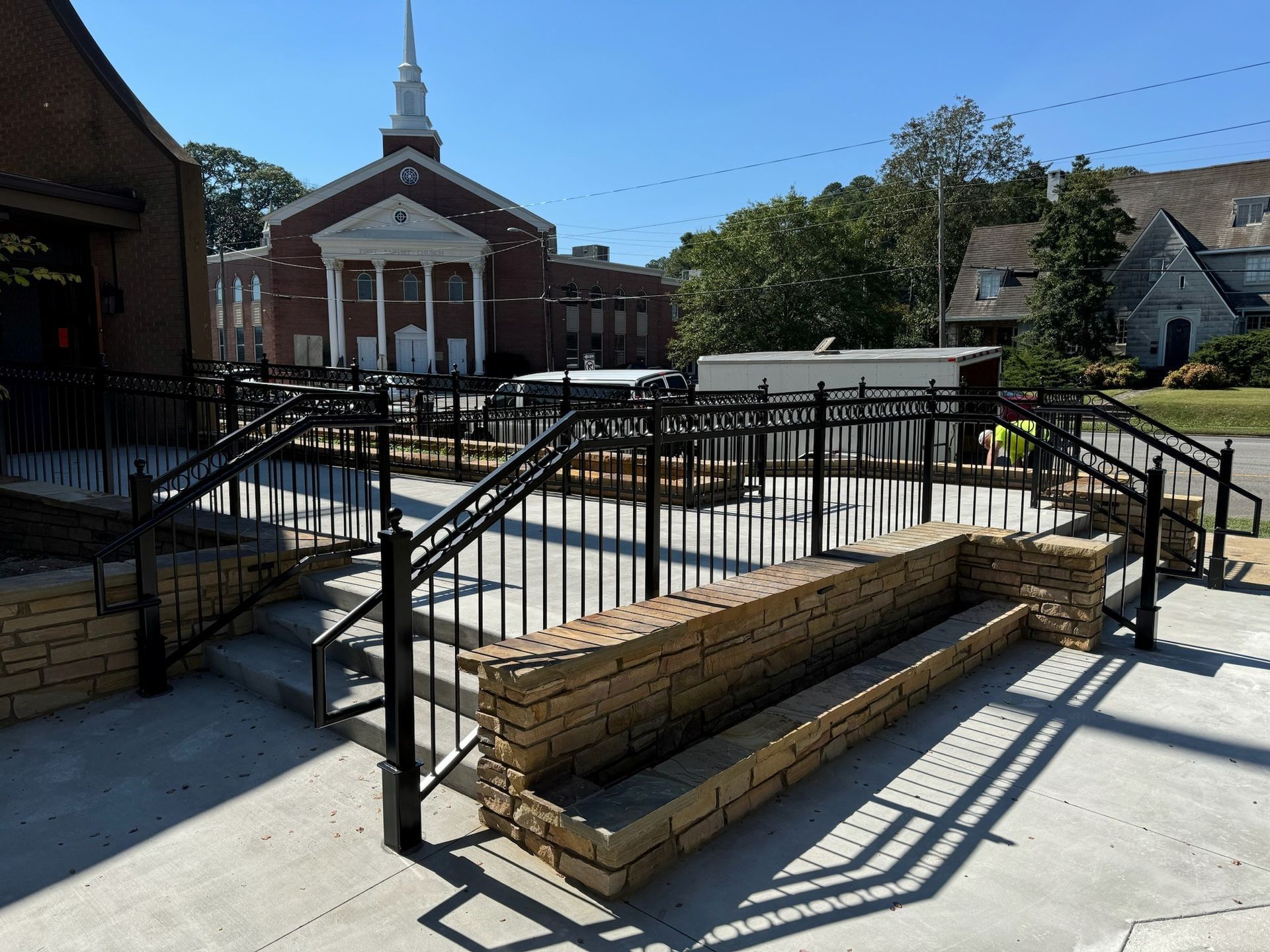 Brick church entrance with black railings and steps in a sunny courtyard