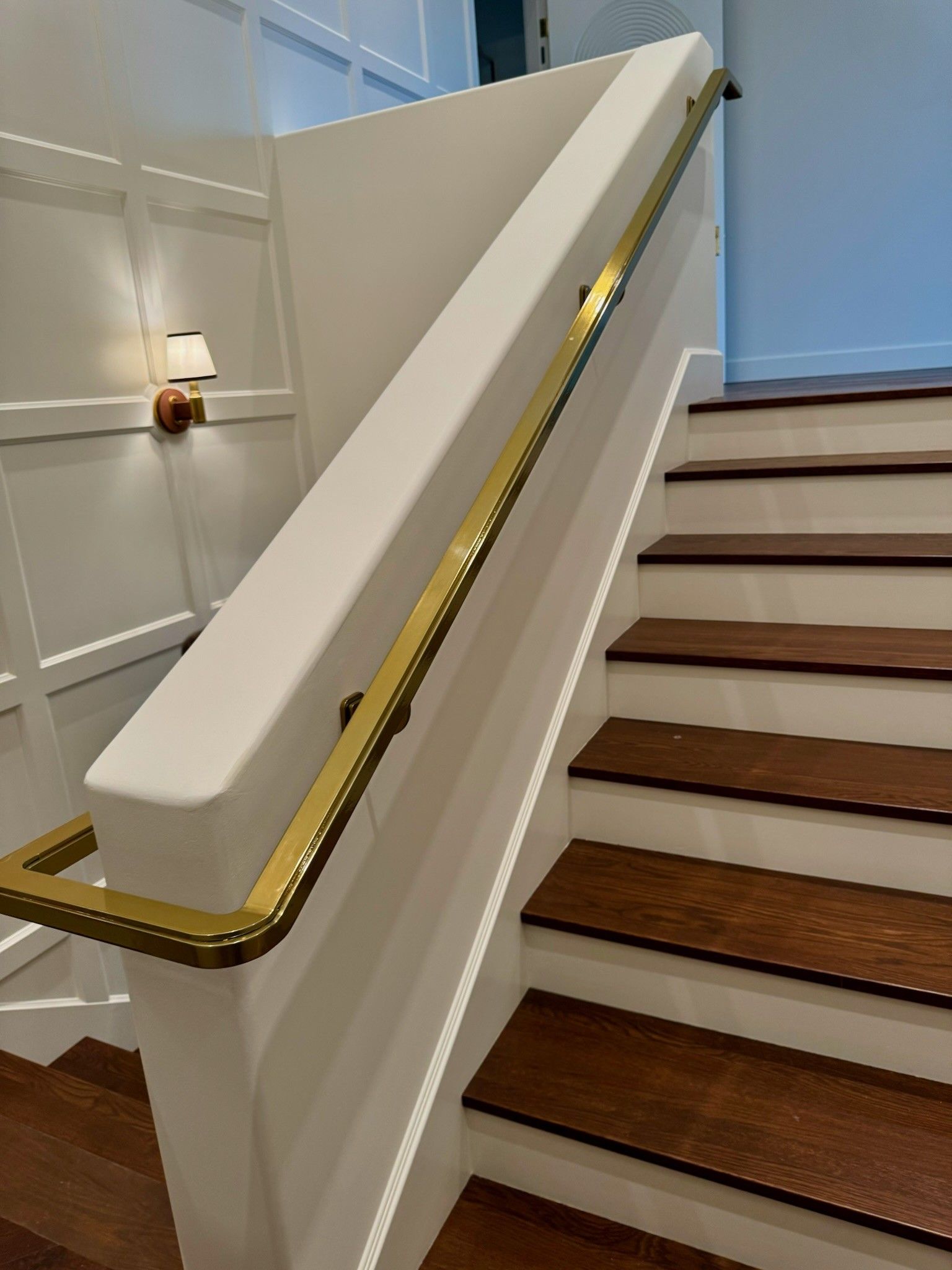 White stairway with wood steps and a gold handrail in a bright interior.