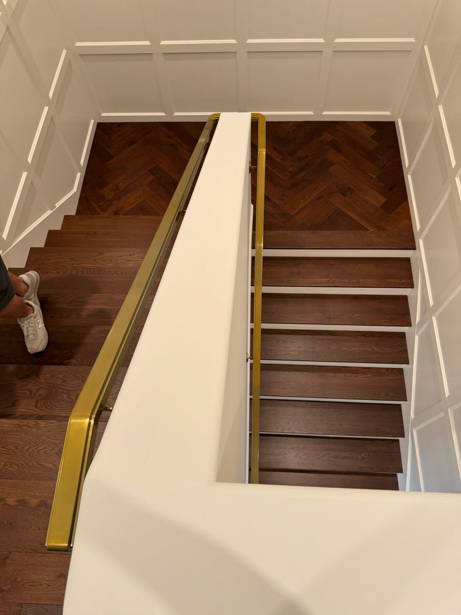 Staircase with dark wood steps, white walls, and a gold handrail viewed from above.