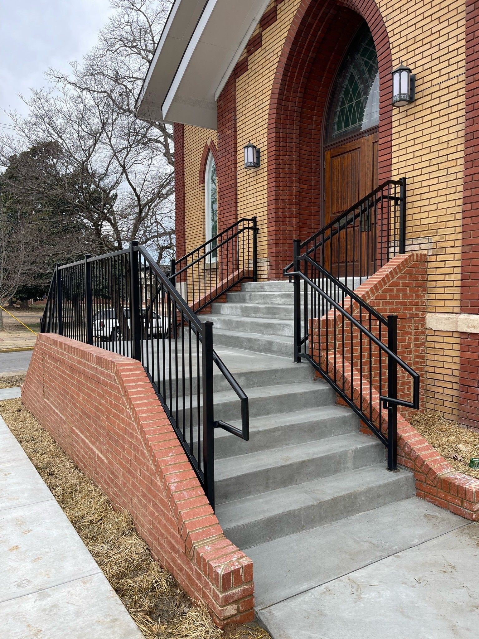 Brick building entrance with concrete steps, black railings, and an accessible ramp beside the stairs