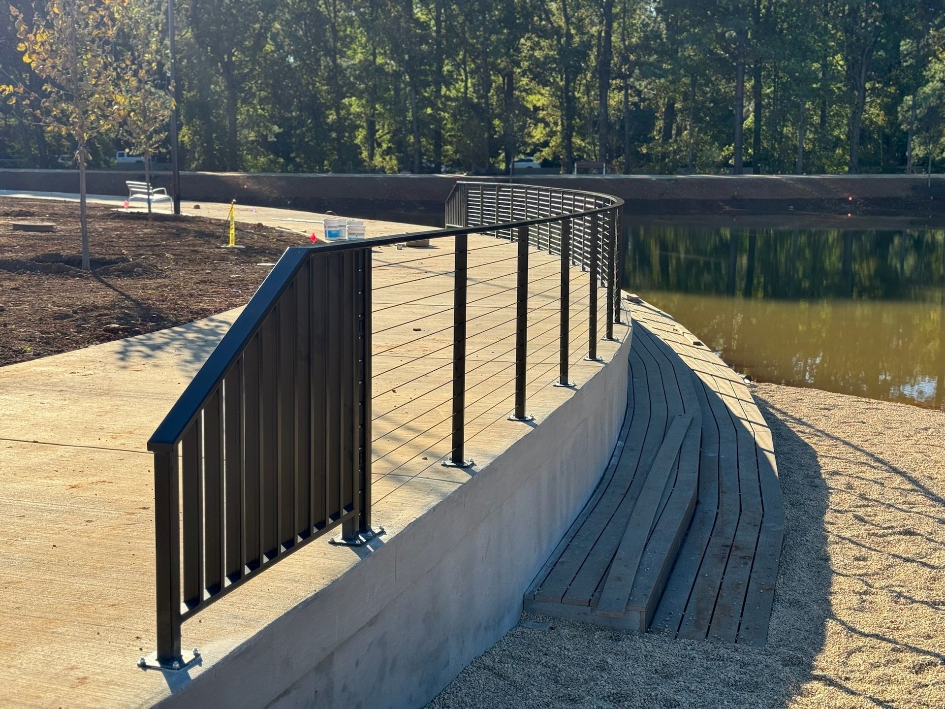 Curved concrete ramp with black metal railings beside a pond and sandy path in a park