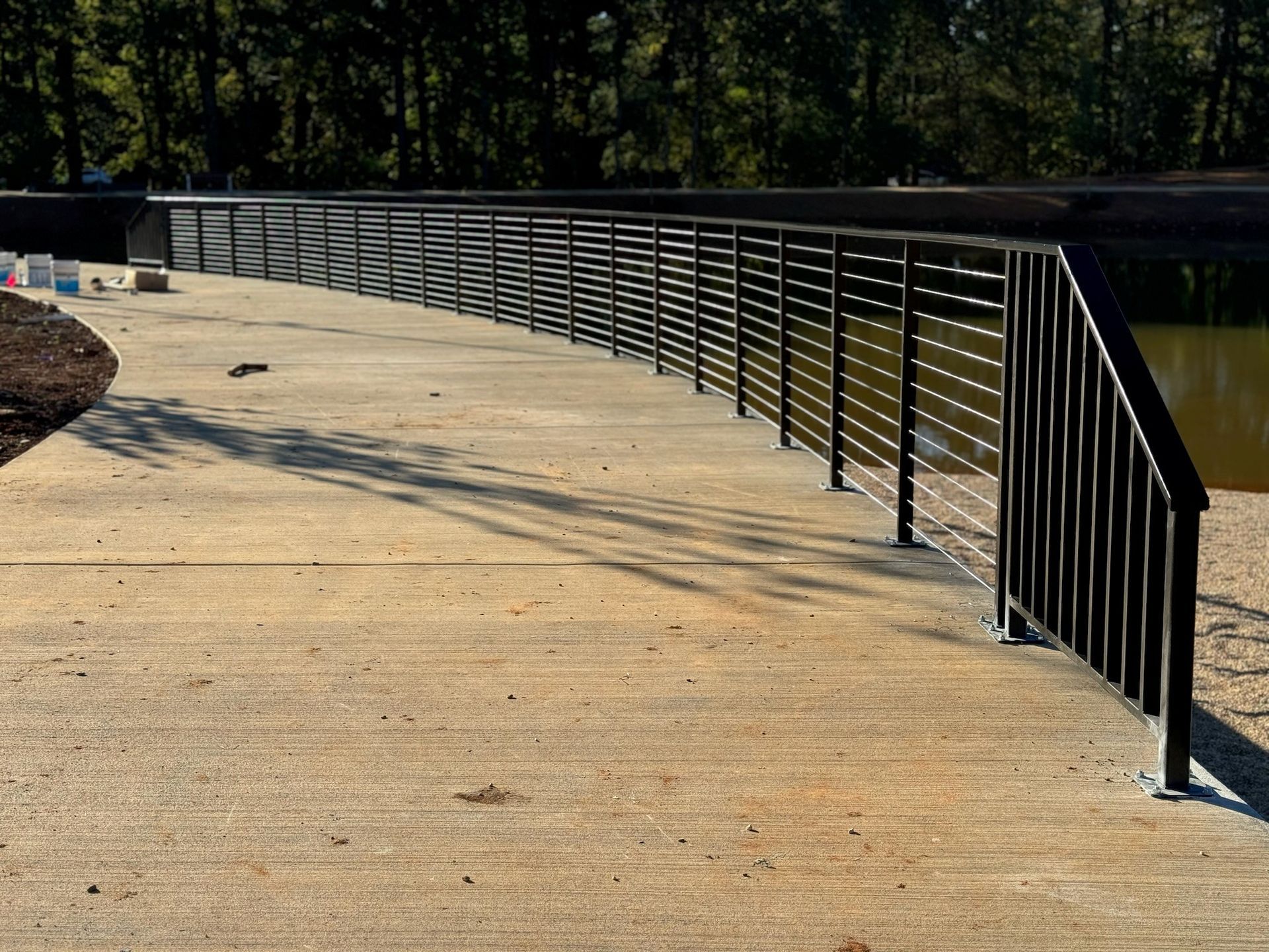 Curved concrete walkway with black metal railing along a waterway in bright sunlight