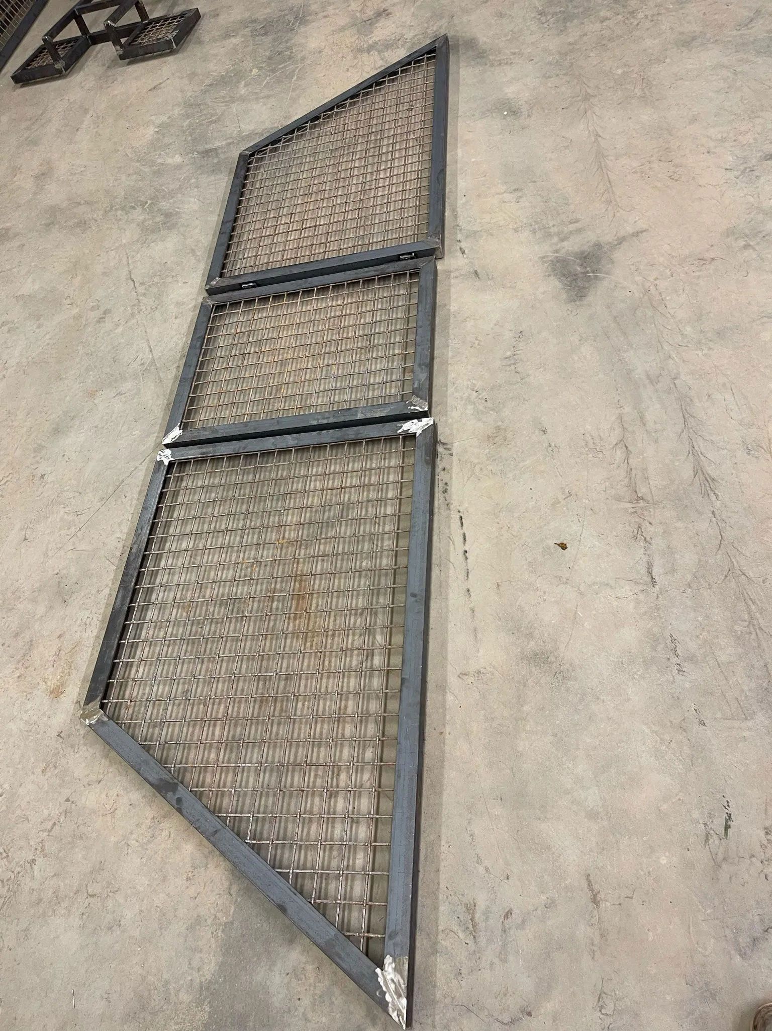 Metal mesh gate panel leaning against a beige wall on a concrete floor.