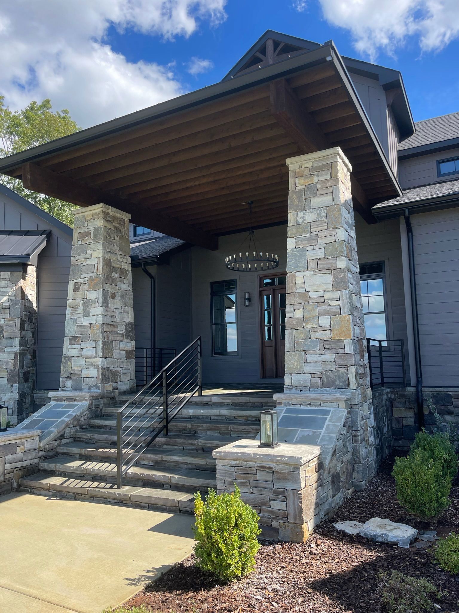 Stone building entrance with covered porch, steps, and handrails under a peaked roof