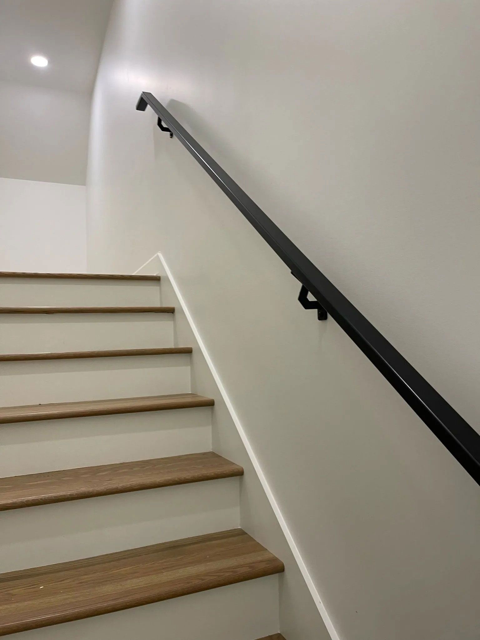 Stairwell with white walls, brown steps, and a black handrail along the right side.