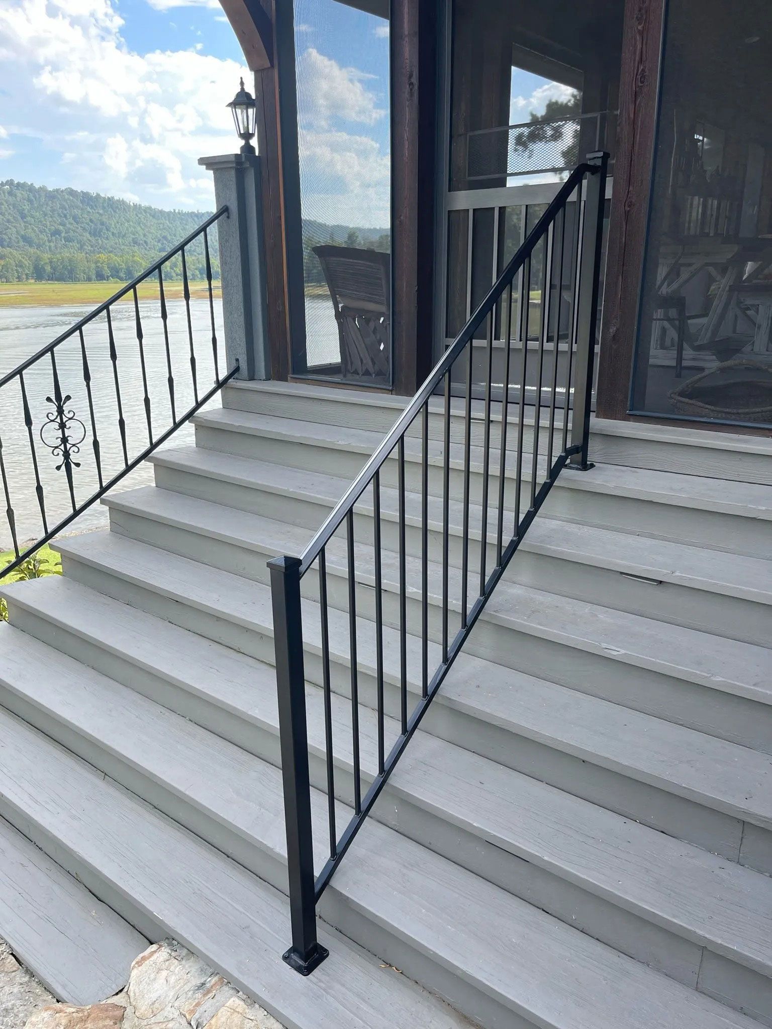 Exterior stairs with black railings leading to a house entrance, with a lake and hills in the background