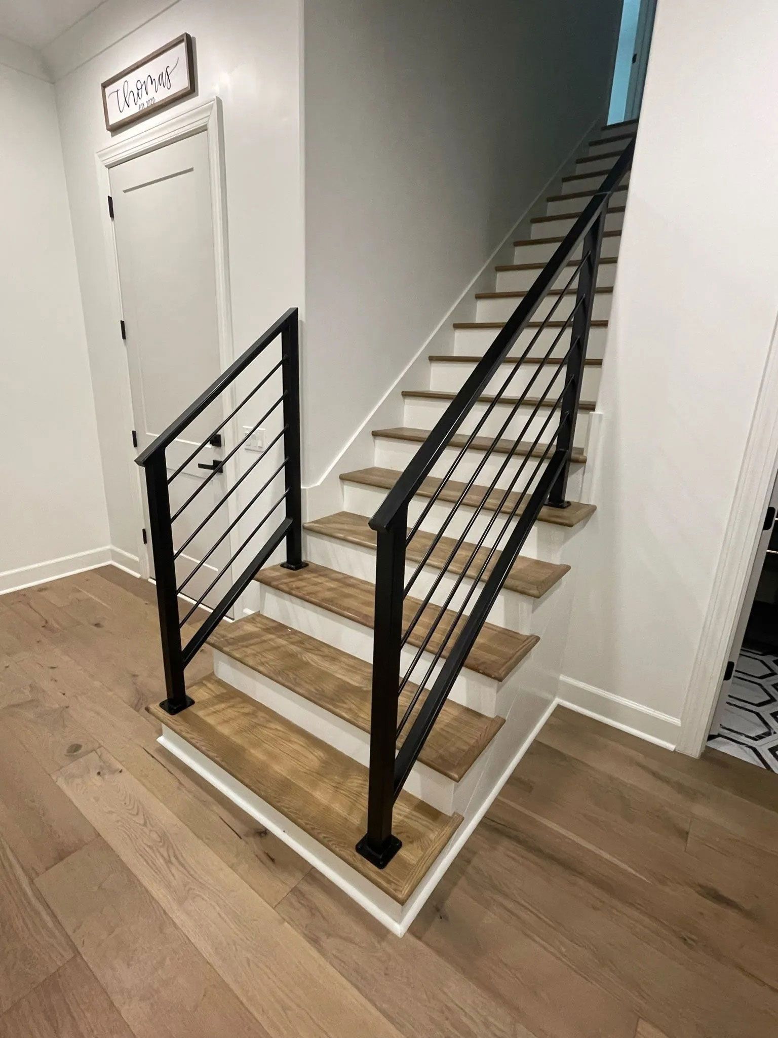 Indoor staircase with black railing, white walls, and wood steps leading upward.