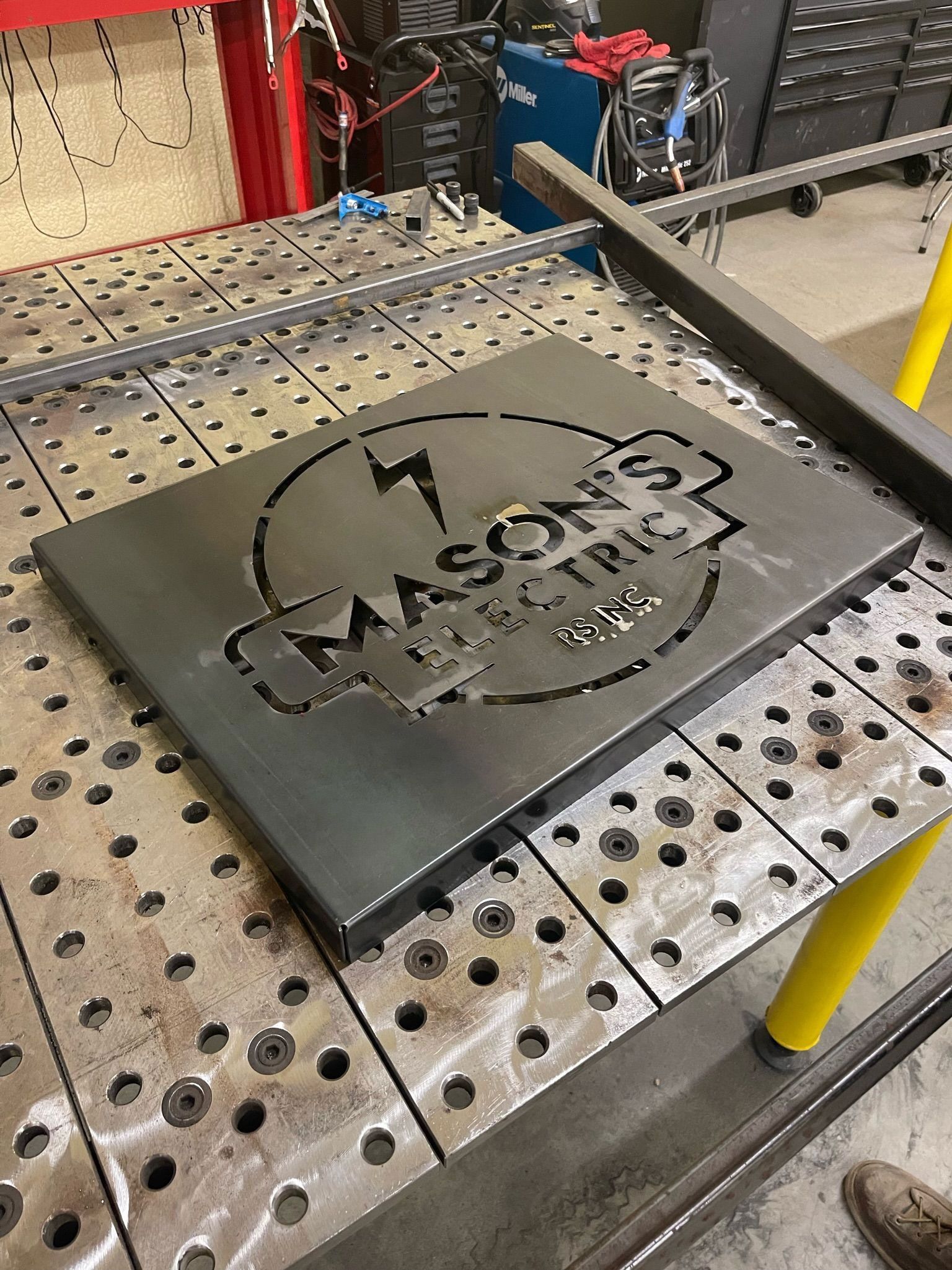 Black metal sign engraved with the Chacon’s logo resting on a perforated workbench in a workshop.