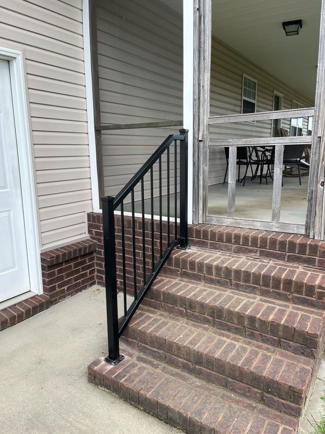 Brick porch steps with black handrail leading to a covered patio and white siding