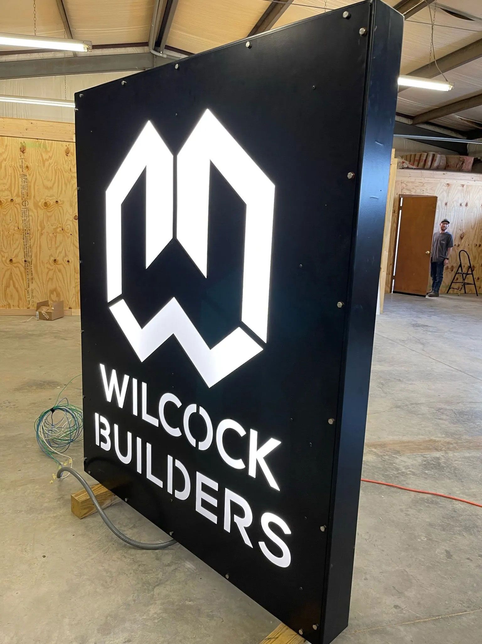 Black Wilcock Builders sign with white logo in an indoor construction site
