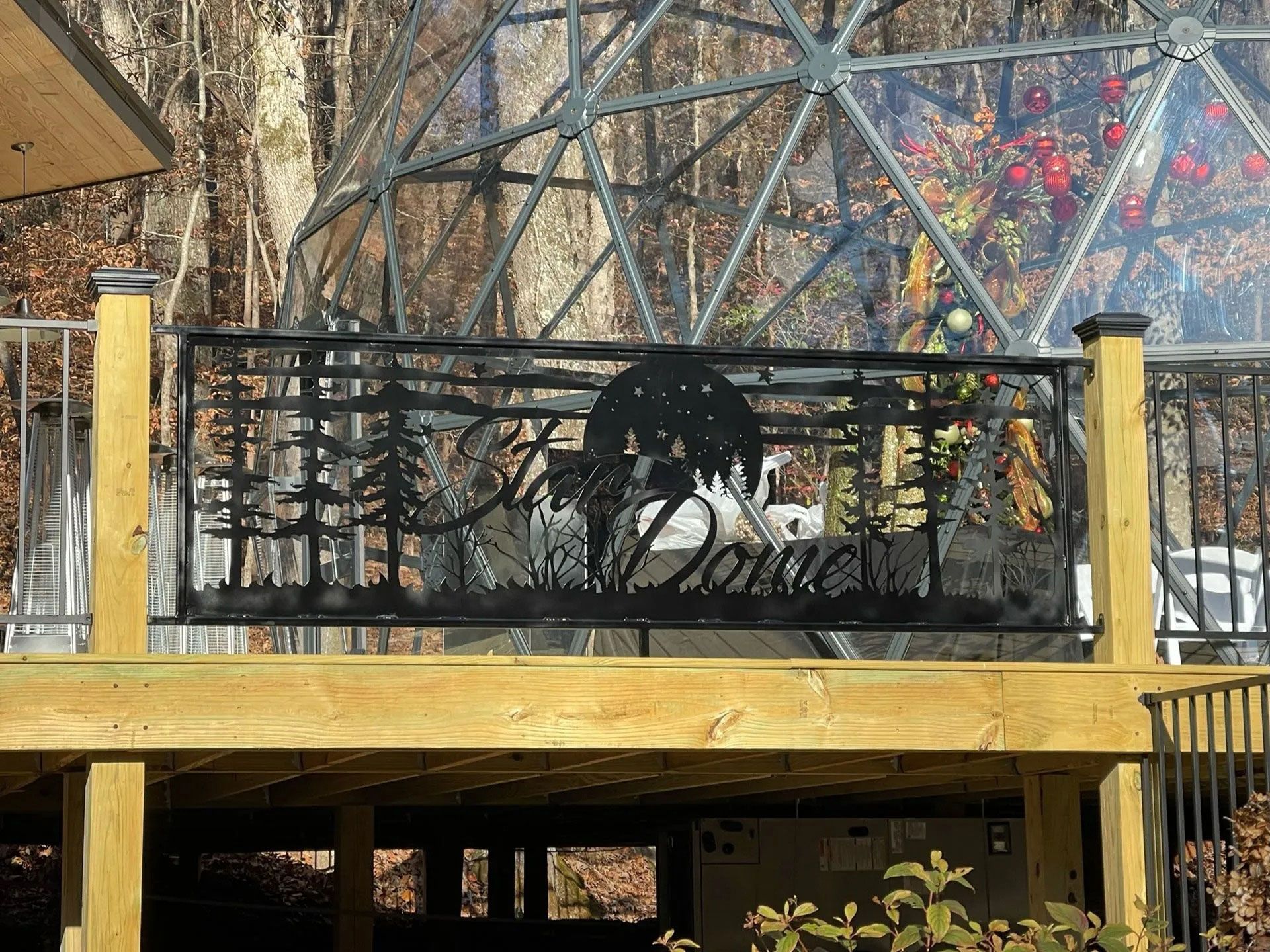 Black metal balcony railing with a spider design in front of a colorful mural and wooden deck