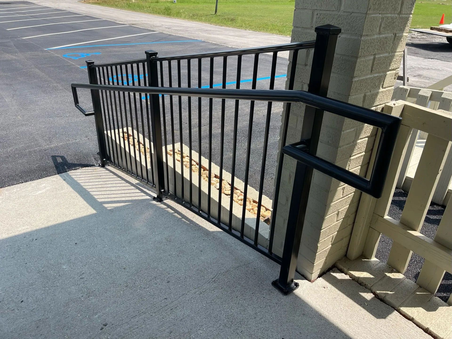 Black metal gate beside a concrete walkway and stone pillar at a driveway entrance.