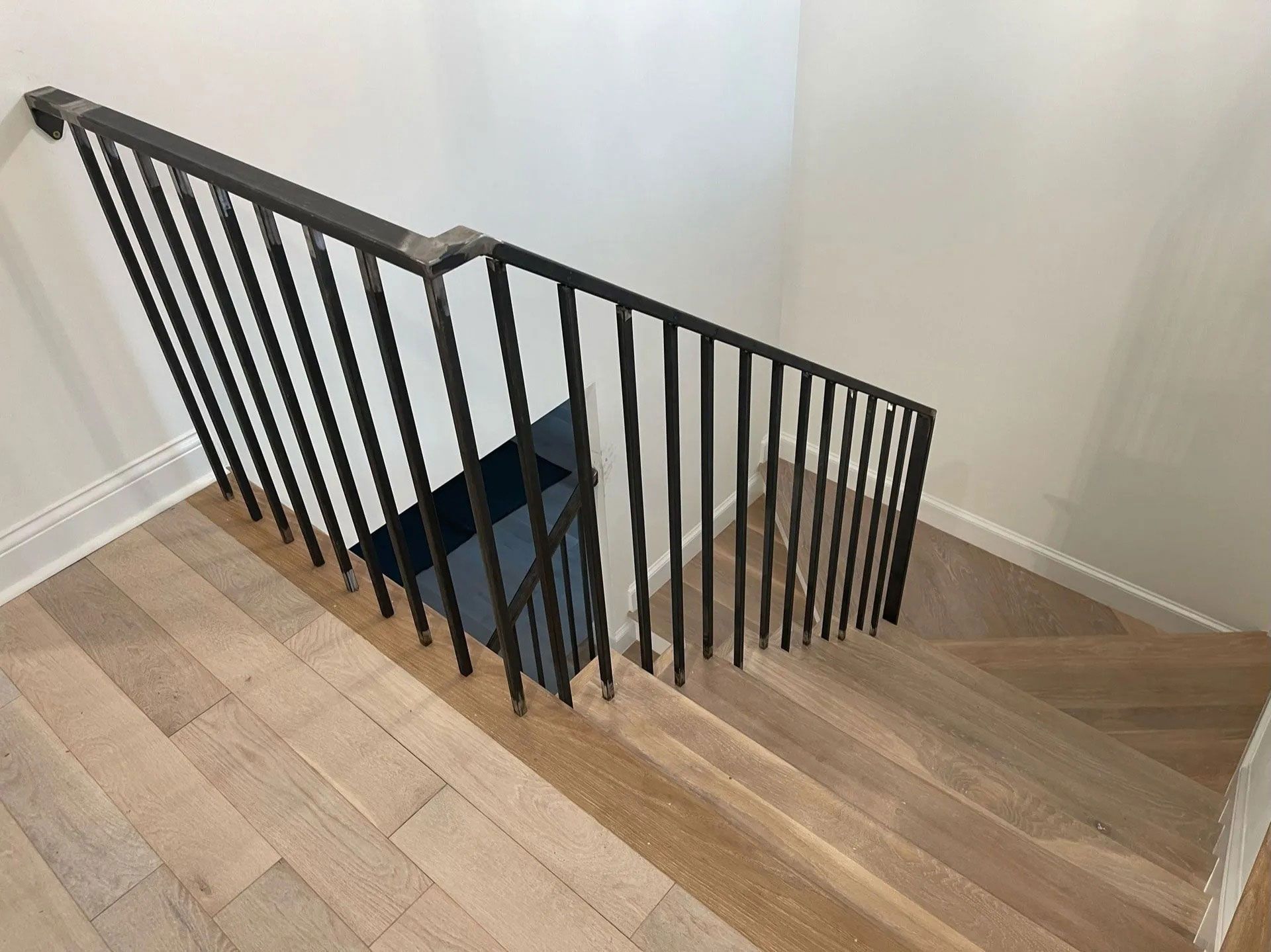 Staircase with black metal railing and wooden steps in a bright indoor hallway