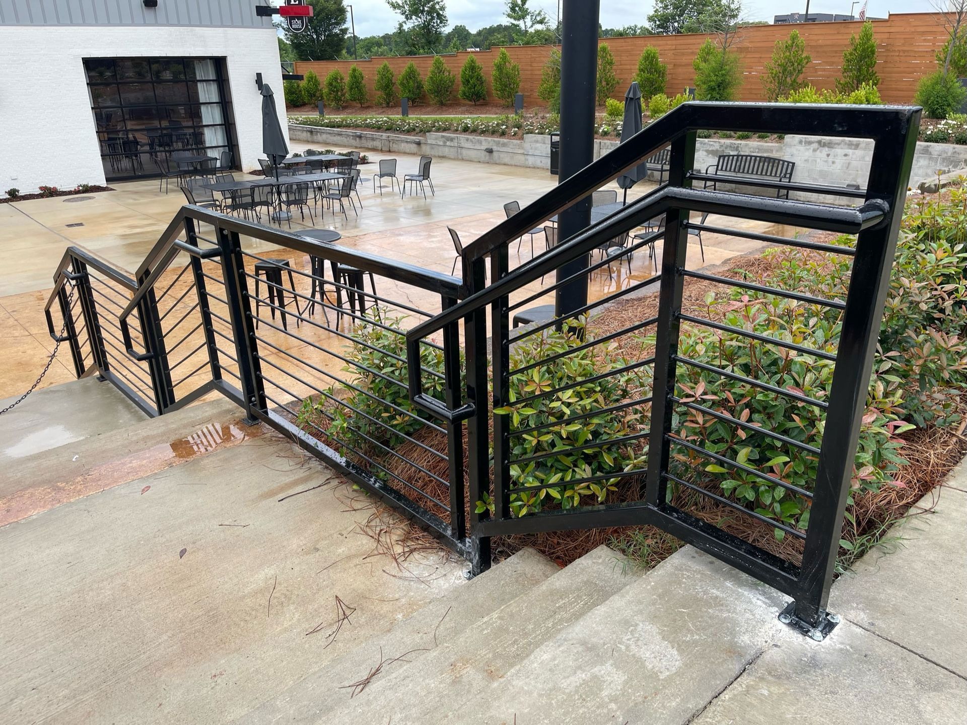 Black metal staircase and ramp with railings leading to a patio in a courtyard, beside a garage and landscaping