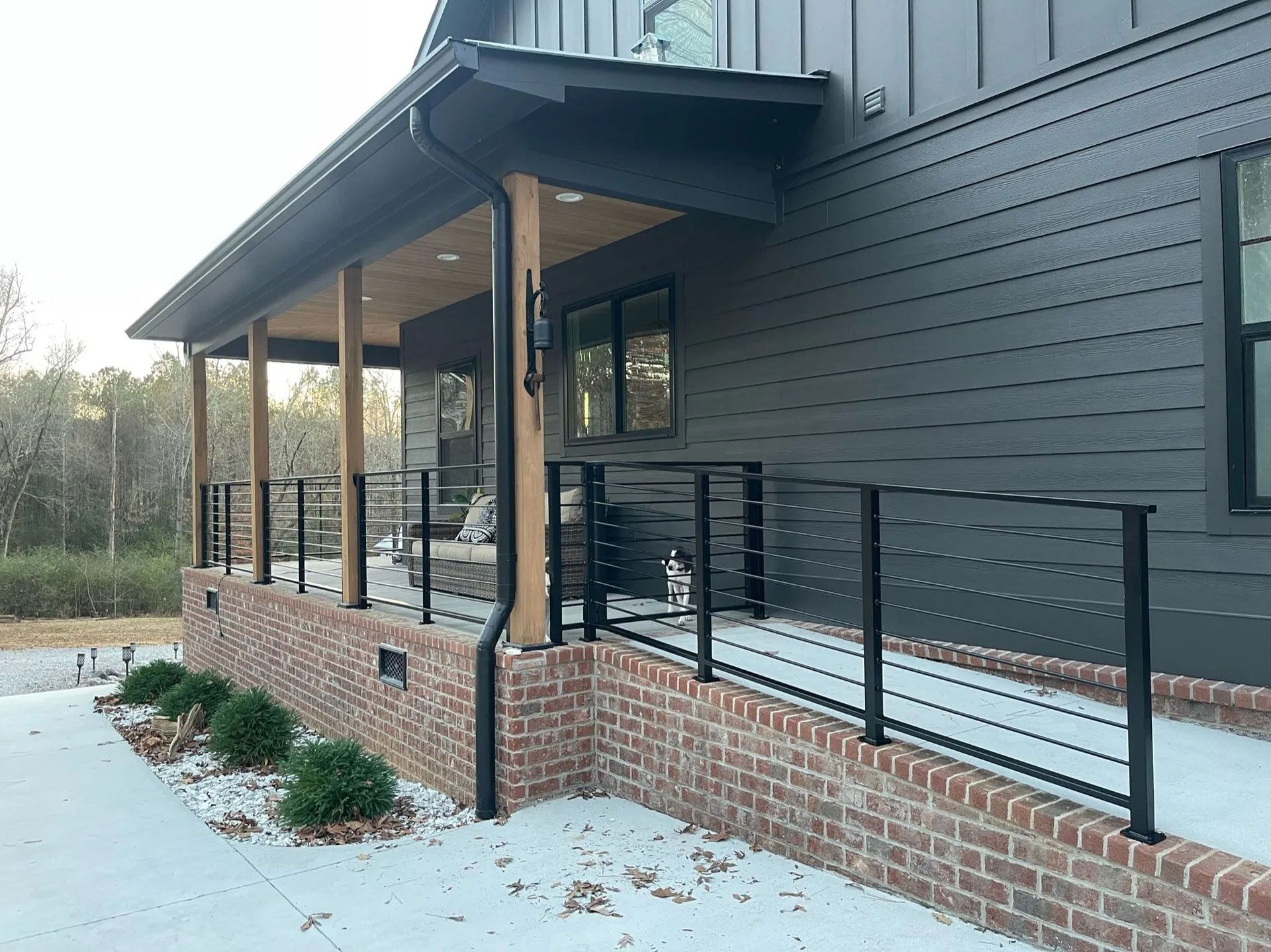 Modern house exterior with black siding, brick base, and covered porch with railing